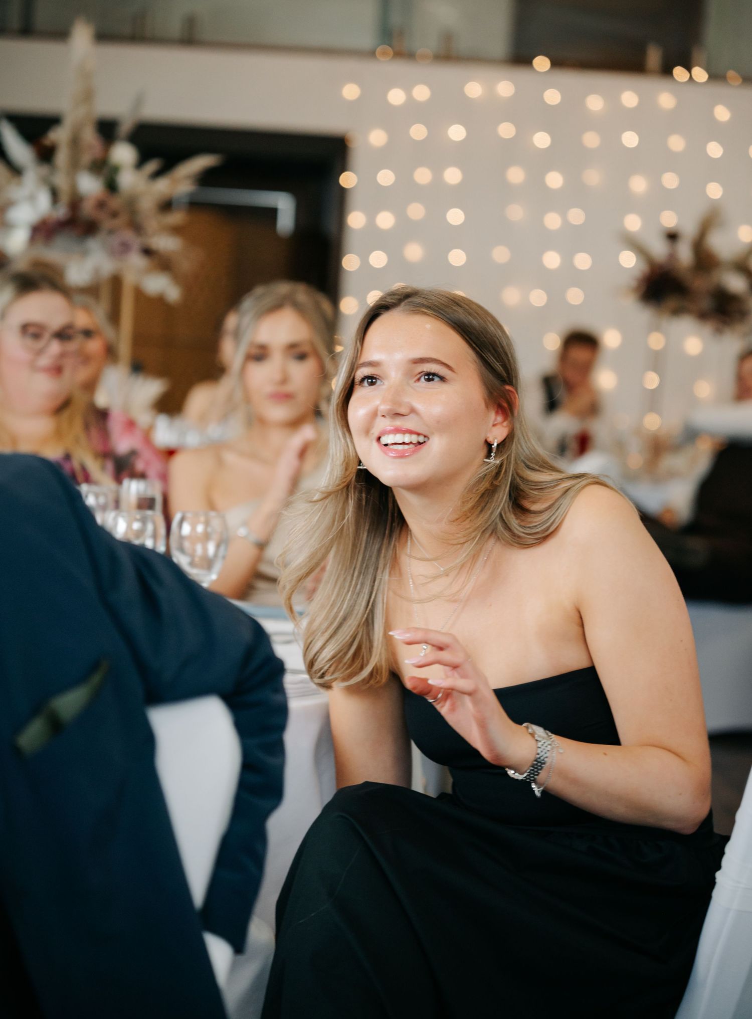 Wedding guests in formal black attire enjoying themselves at an evening reception with string lights.