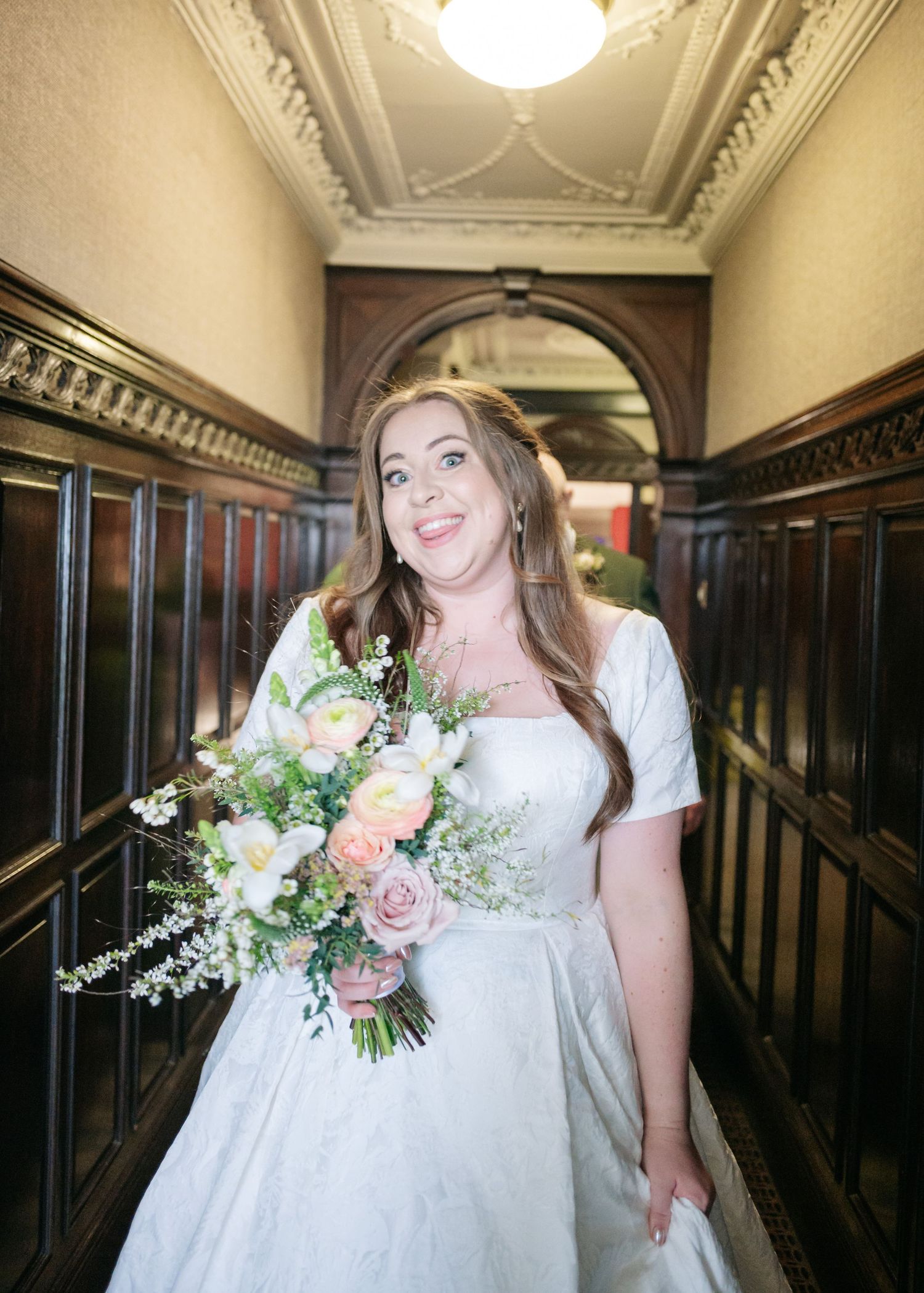 Wedding party walking down an ornate hallway with decorative molding and vintage lighting.