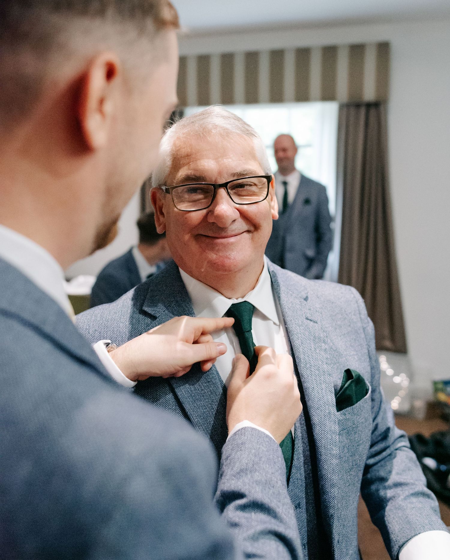 Groomsmen help adjust ties and boutonnieres while getting ready in formal grey suits.