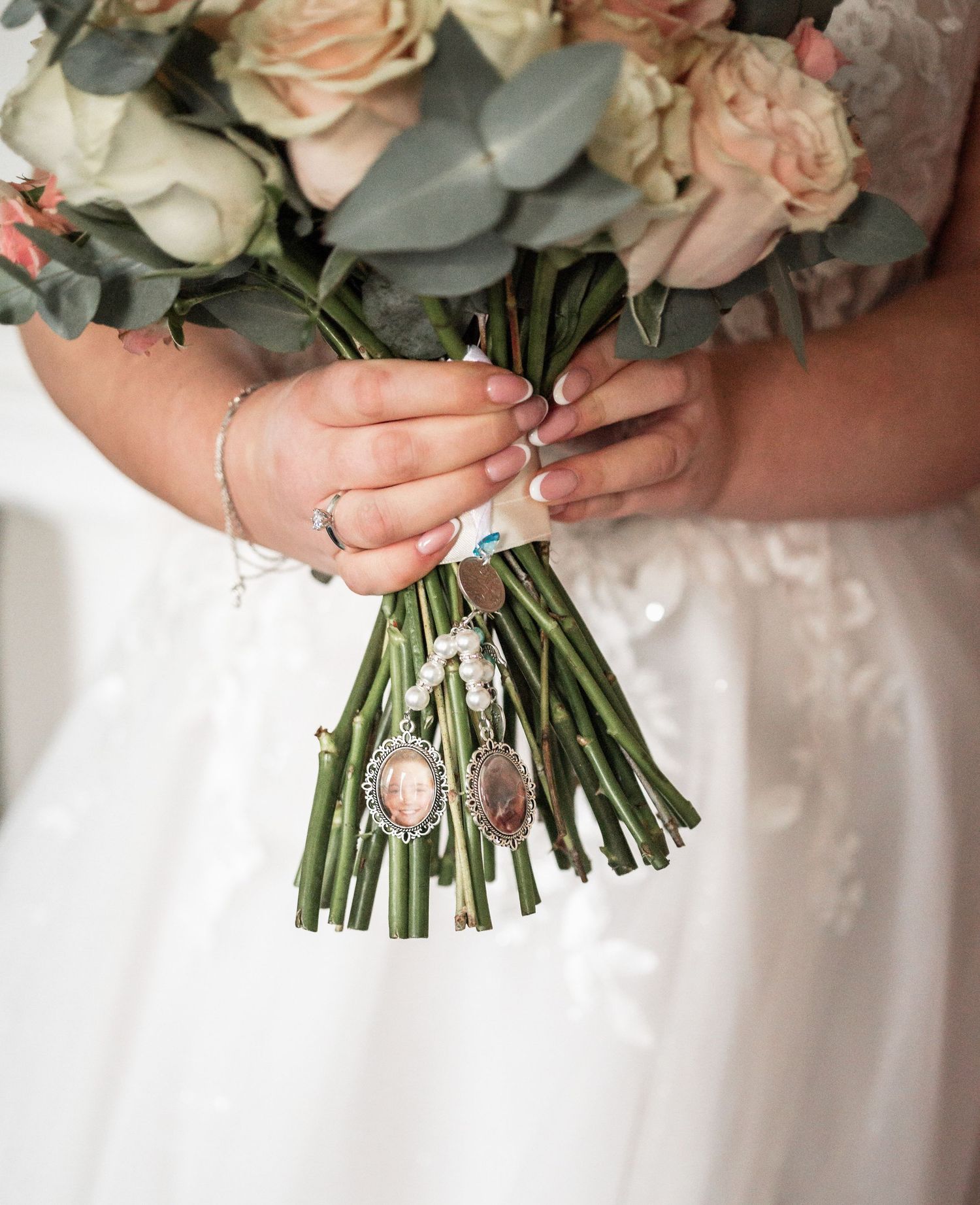 Close up of bridal bouquet with blush roses and silver charms wrapped in white ribbon.