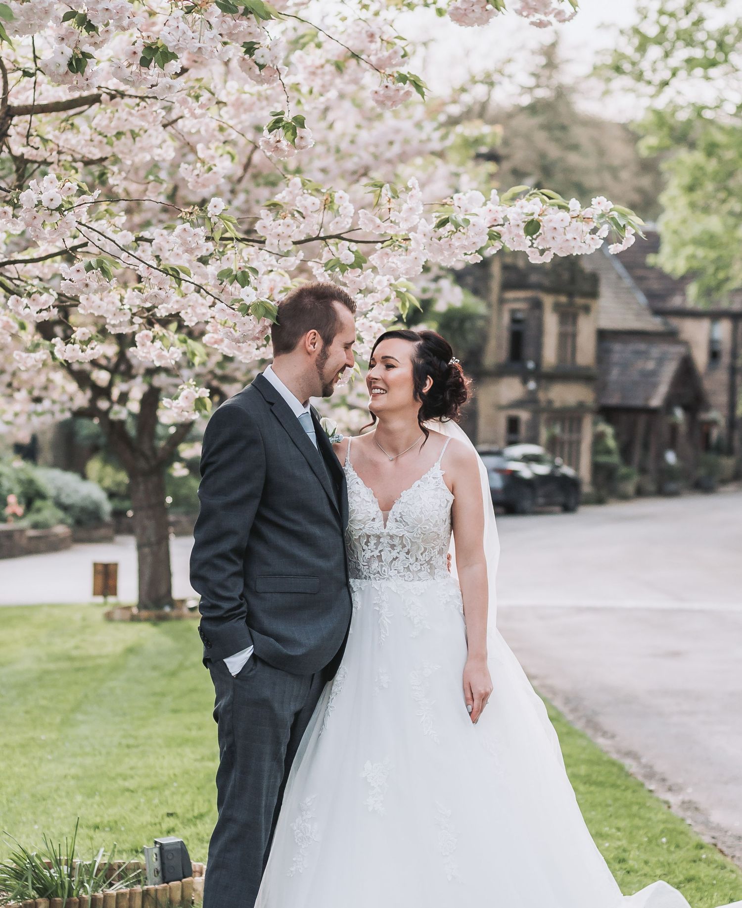 A blissful springtime wedding moment under blooming cherry blossoms with a classic stone building in the background.