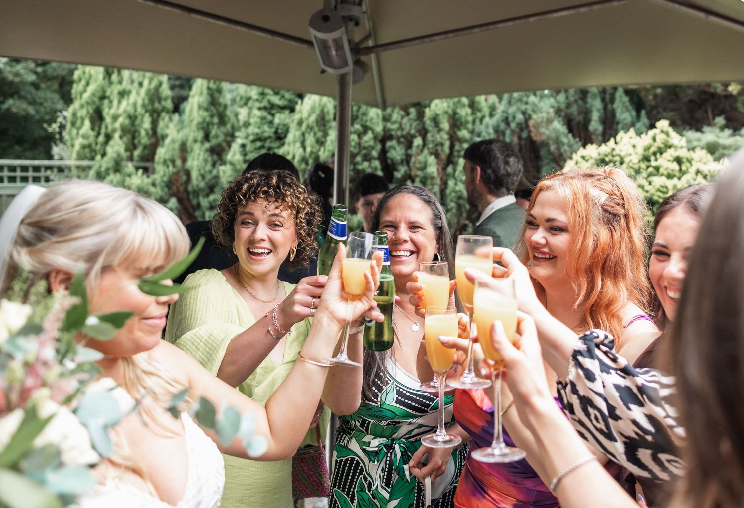 Wedding guests toasting and laughing at an outdoor reception under a tent.