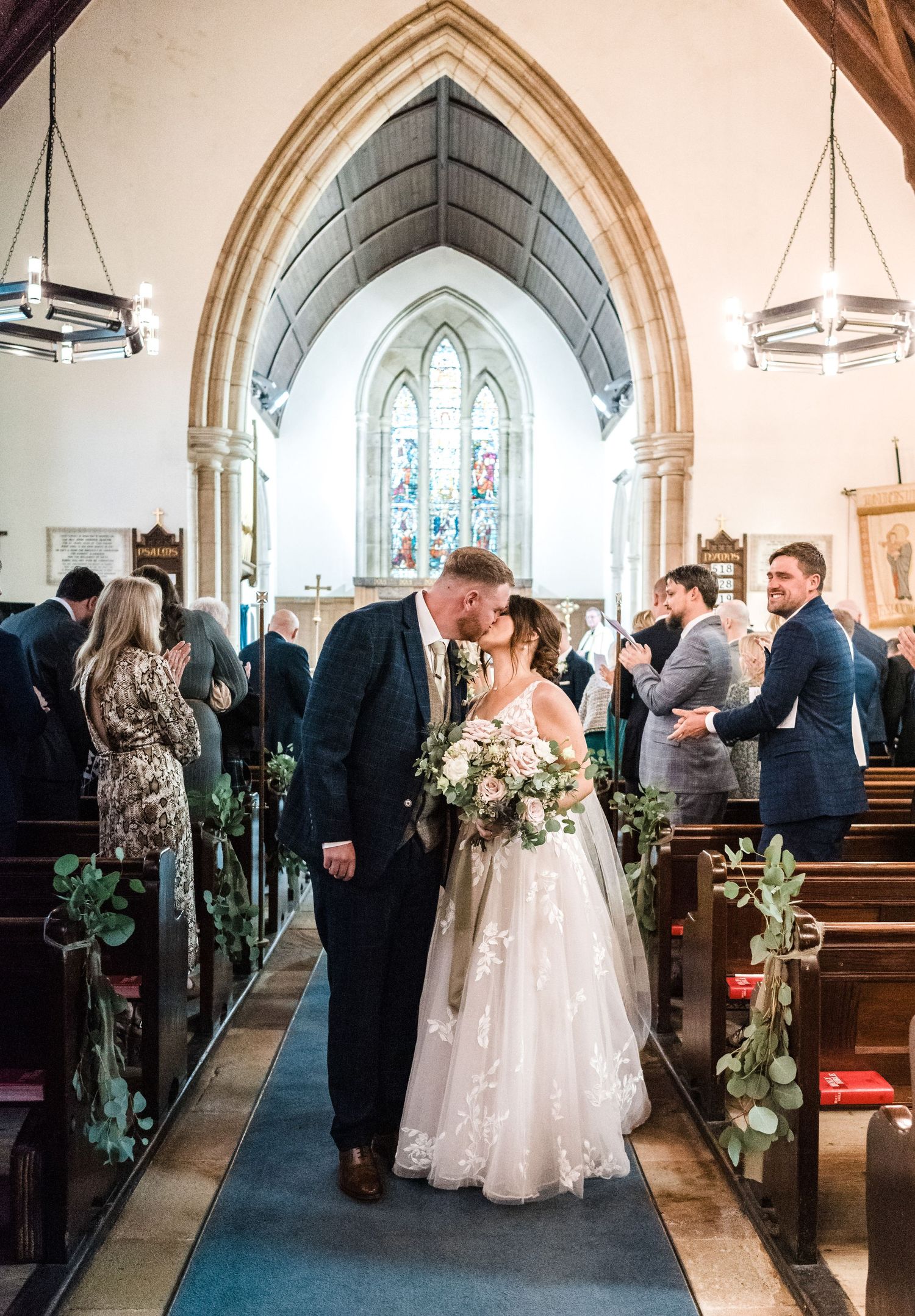 Wedding ceremony in church with Gothic arches and aisle decorated with greenery.
