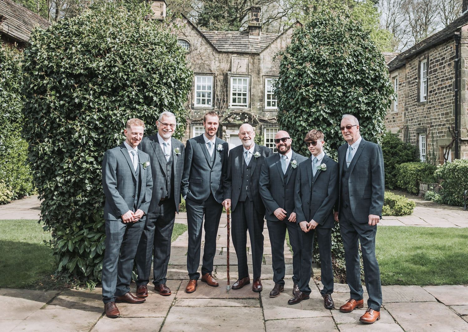 Groomsmen in matching gray suits pose together in front of a stone building.