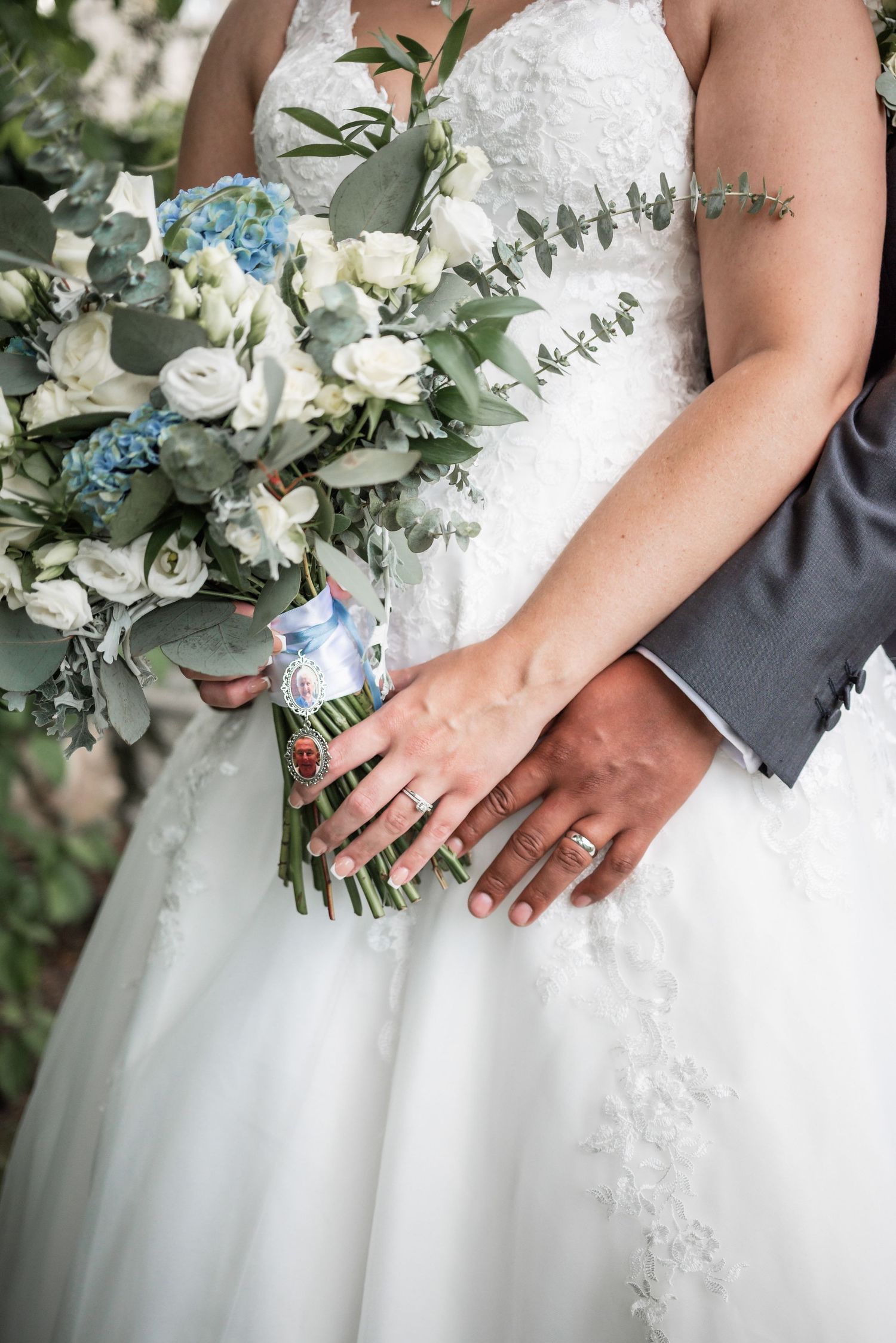 Close-up of hands holding a beautiful white and blue wedding bouquet with eucalyptus accents.
