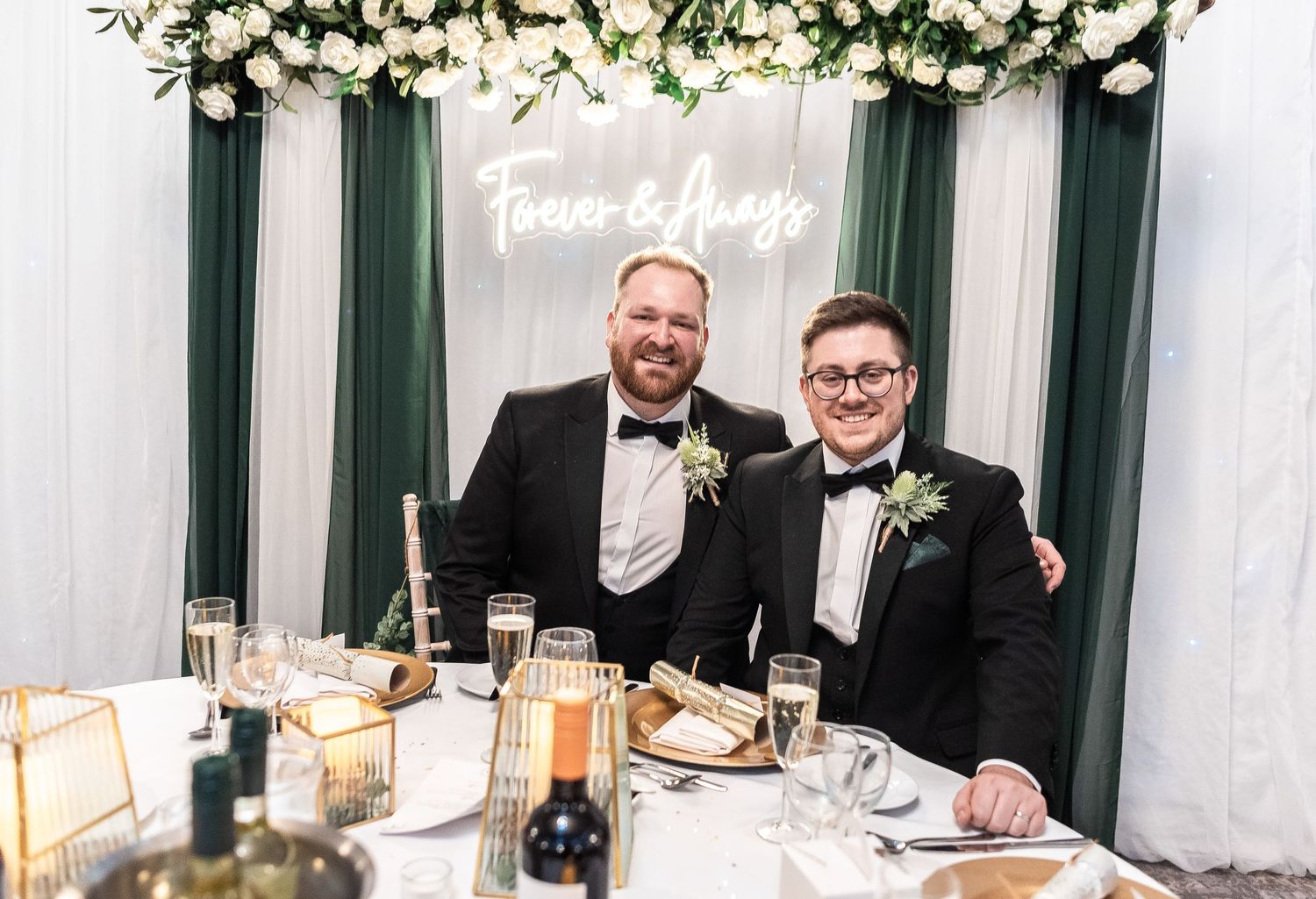 Formal dinner table setting with neon sign and floral backdrop at wedding reception.