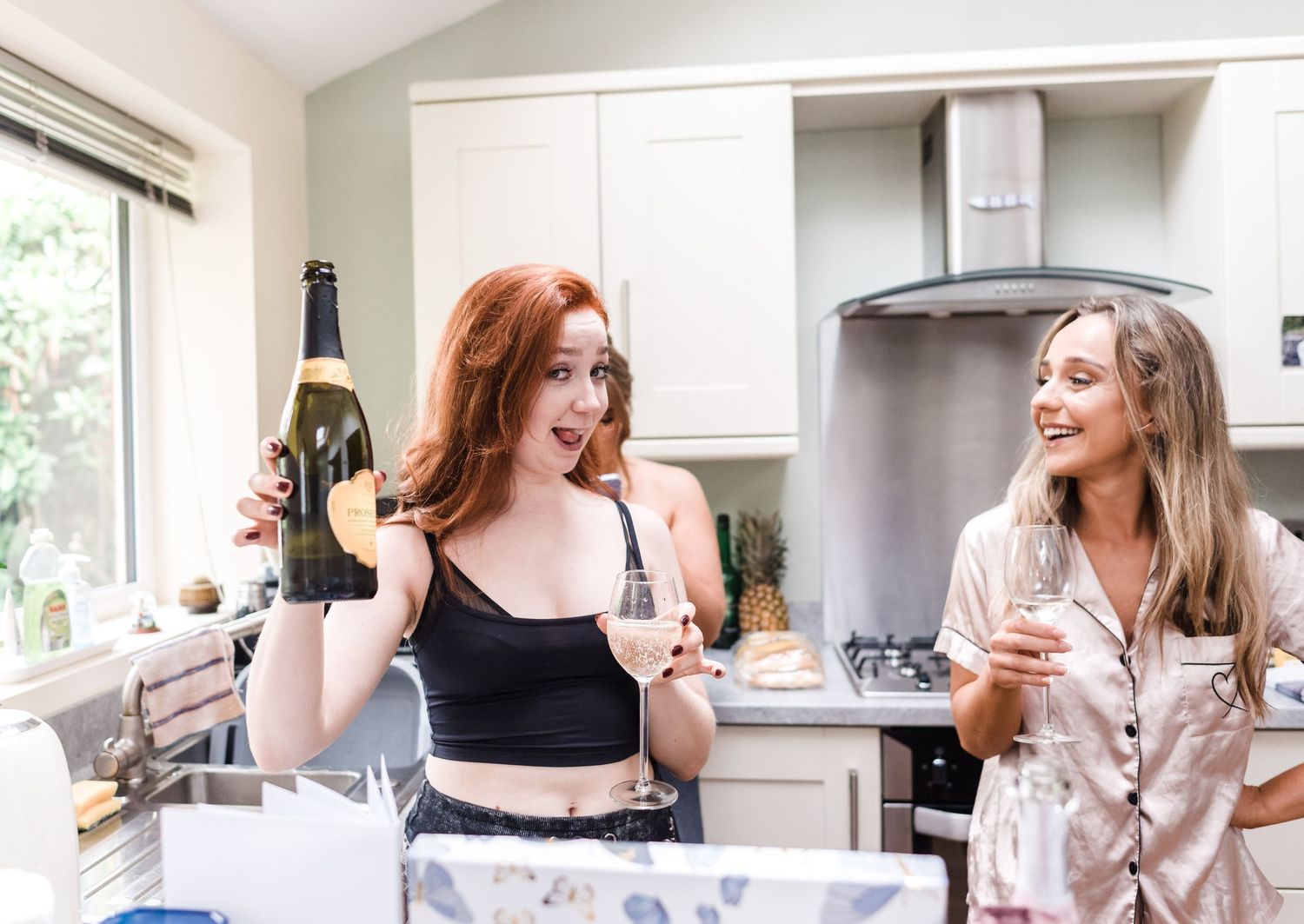 Two friends enjoying wine and laughter together in a modern white kitchen.