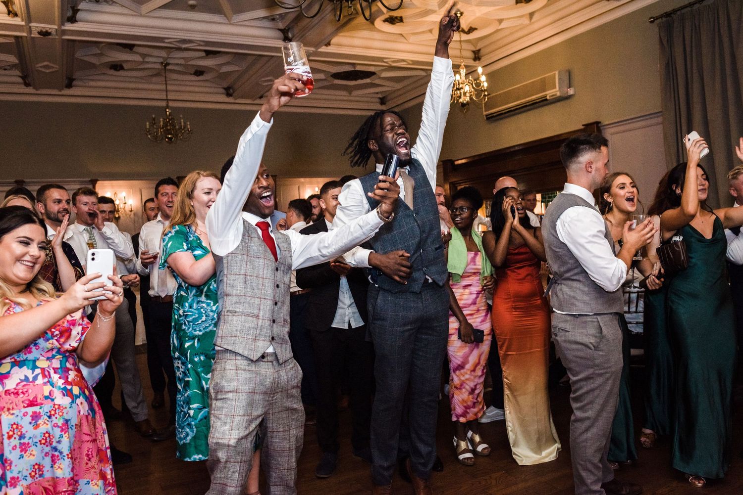 Excited wedding guests raising glasses and celebrating on dance floor.