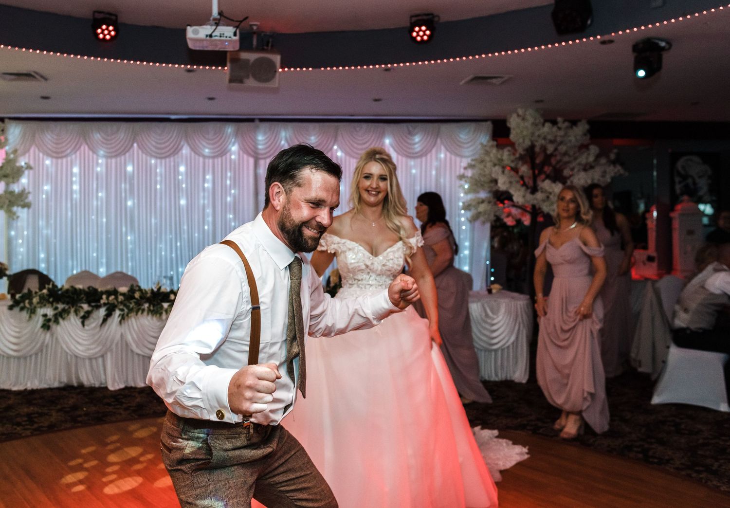 A couple dancing together at their wedding reception with pink lighting and decor.