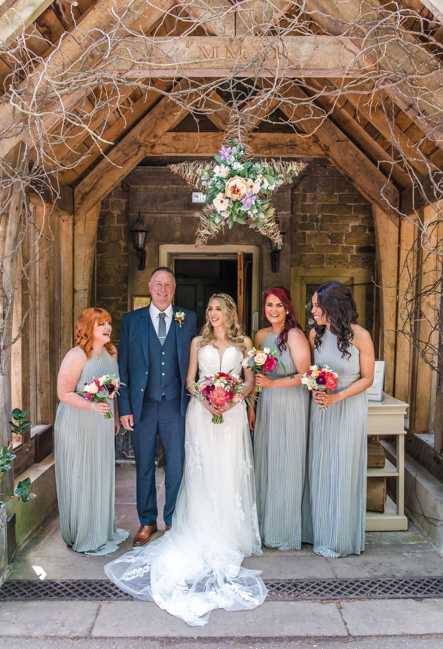 Wedding party poses under floral star arch in stone doorway.