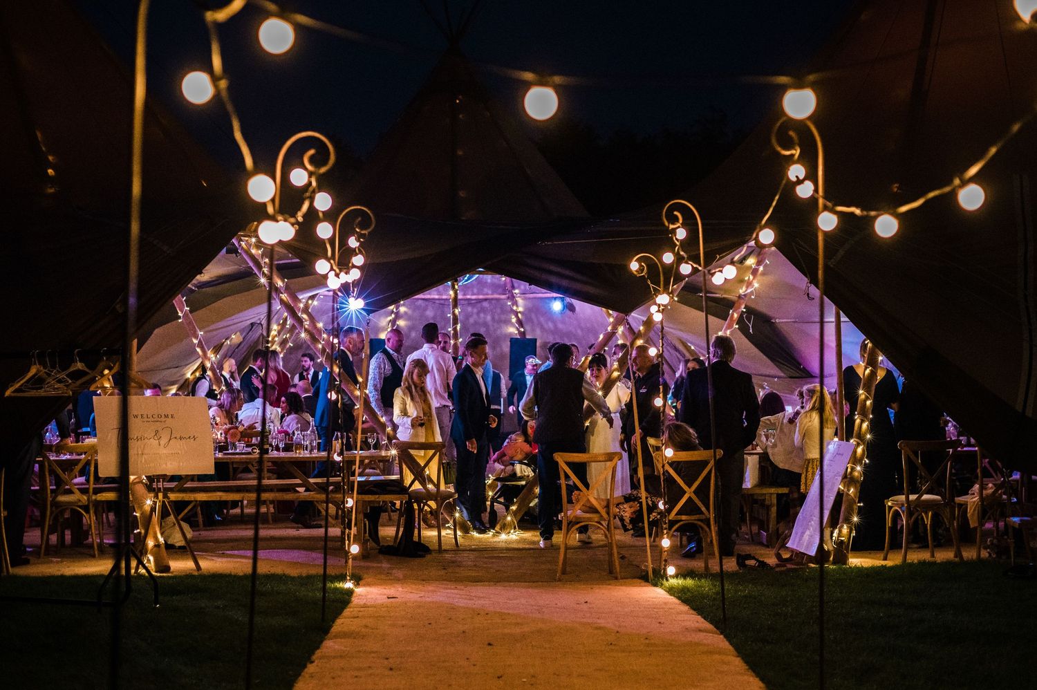 Outdoor wedding tent illuminated at night with string lights creating a magical atmosphere.