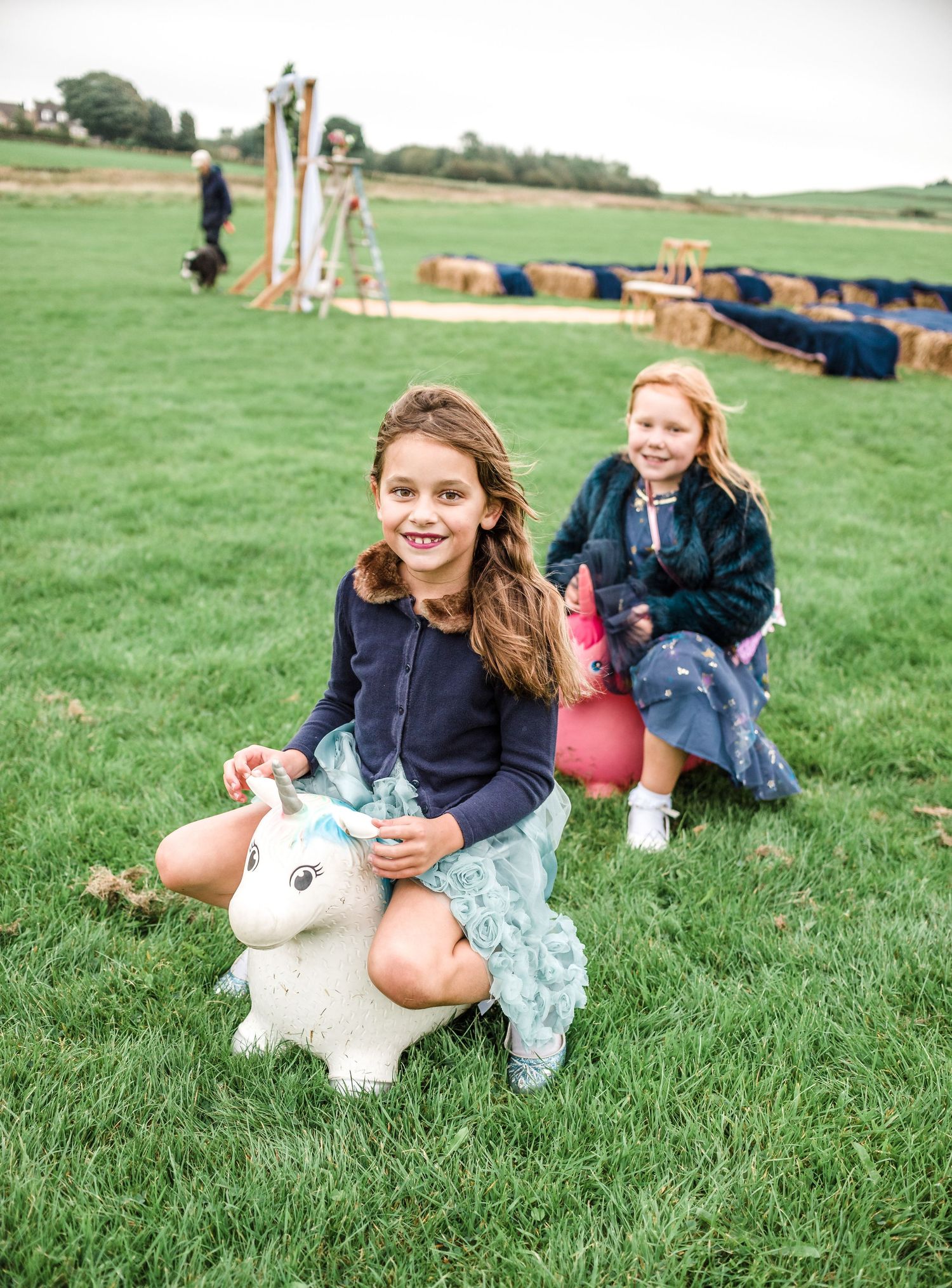 Children playing on inflatable unicorn toys on grassy field at outdoor event.