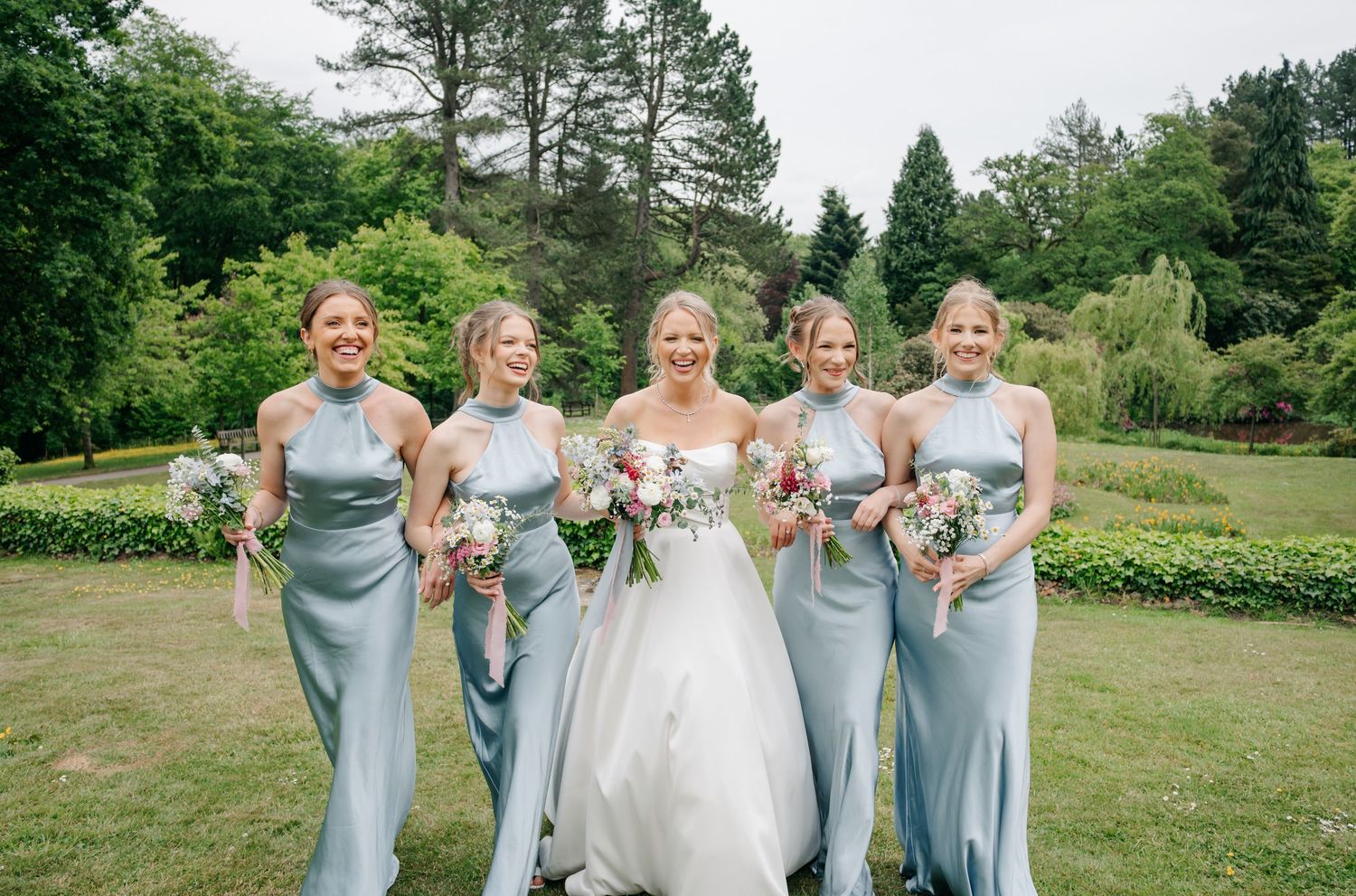 Wedding party in pale blue bridesmaid dresses posing together on lawn.