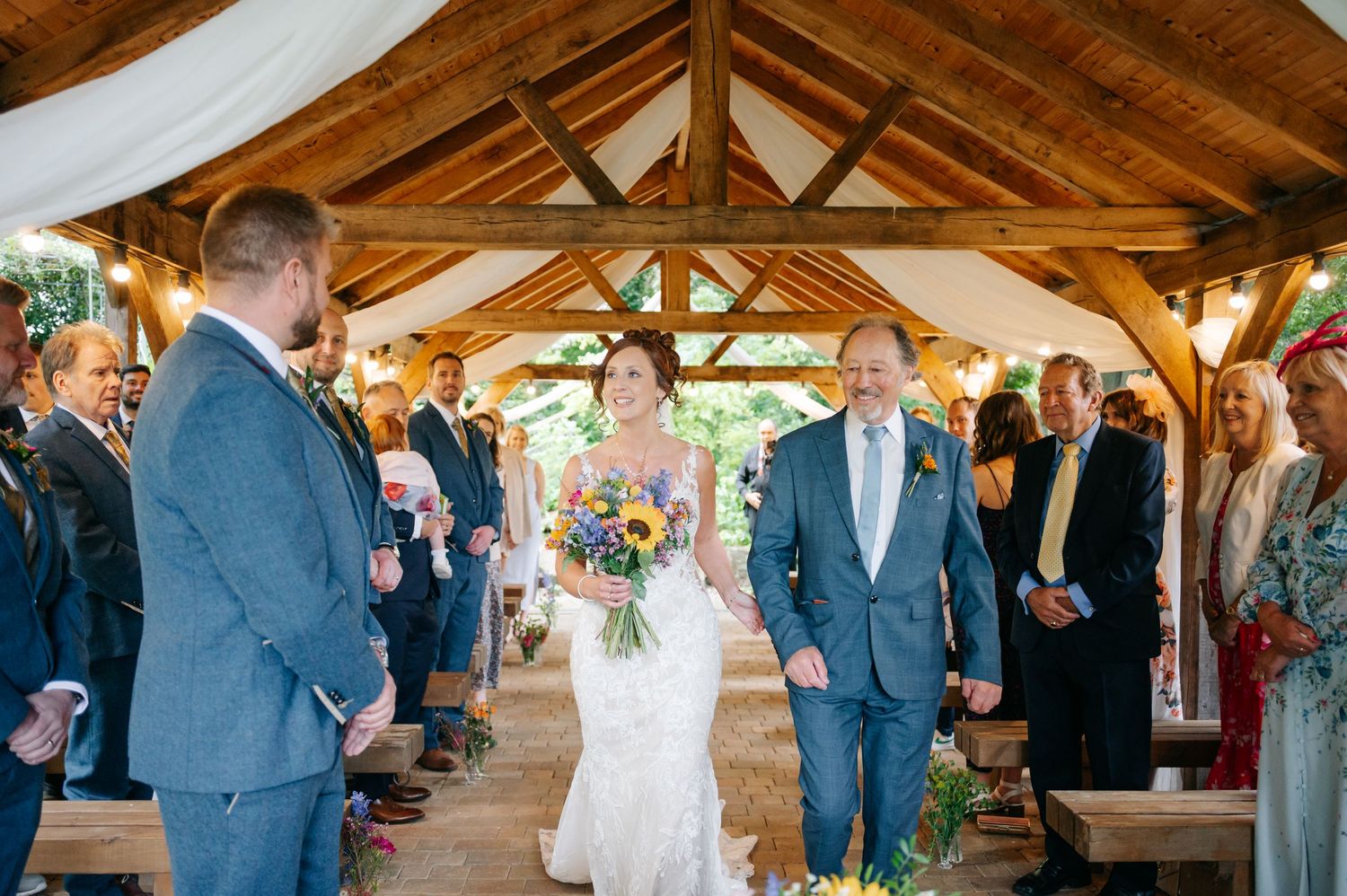 Wedding ceremony taking place in a rustic wooden pavilion with exposed beam ceilings and natural lighting.