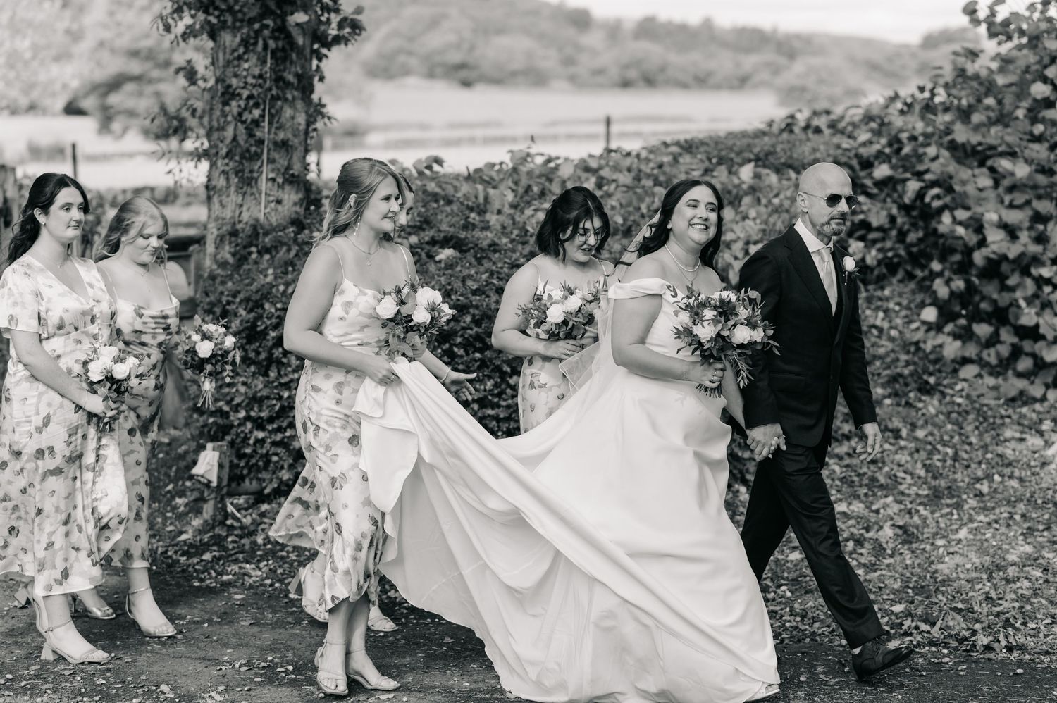 Wedding party poses in a scenic garden setting with flowing white dresses and formal attire creating an elegant atmosphere.