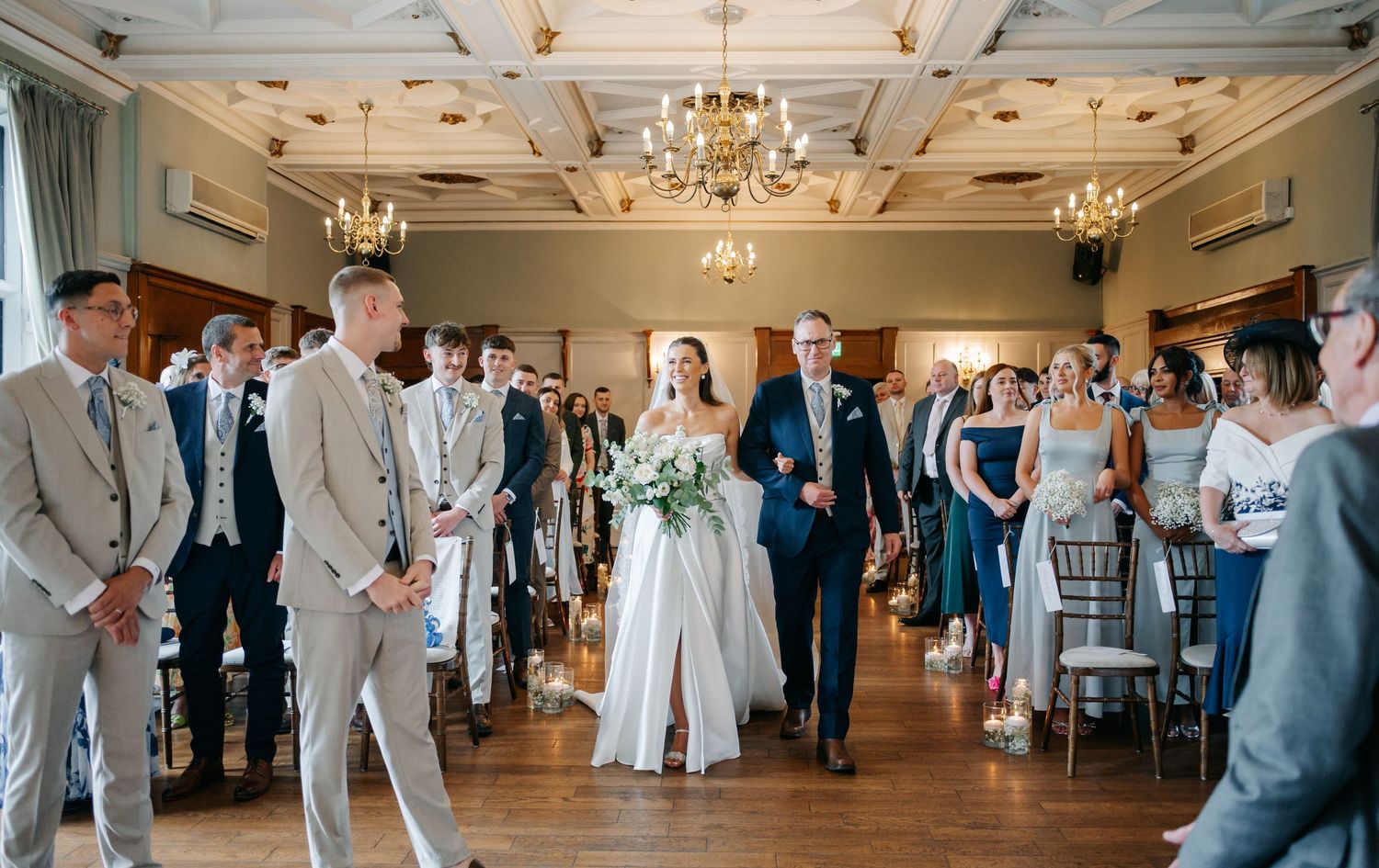 Reception hall decorated with chandeliers and filled with wedding guests in formal attire.