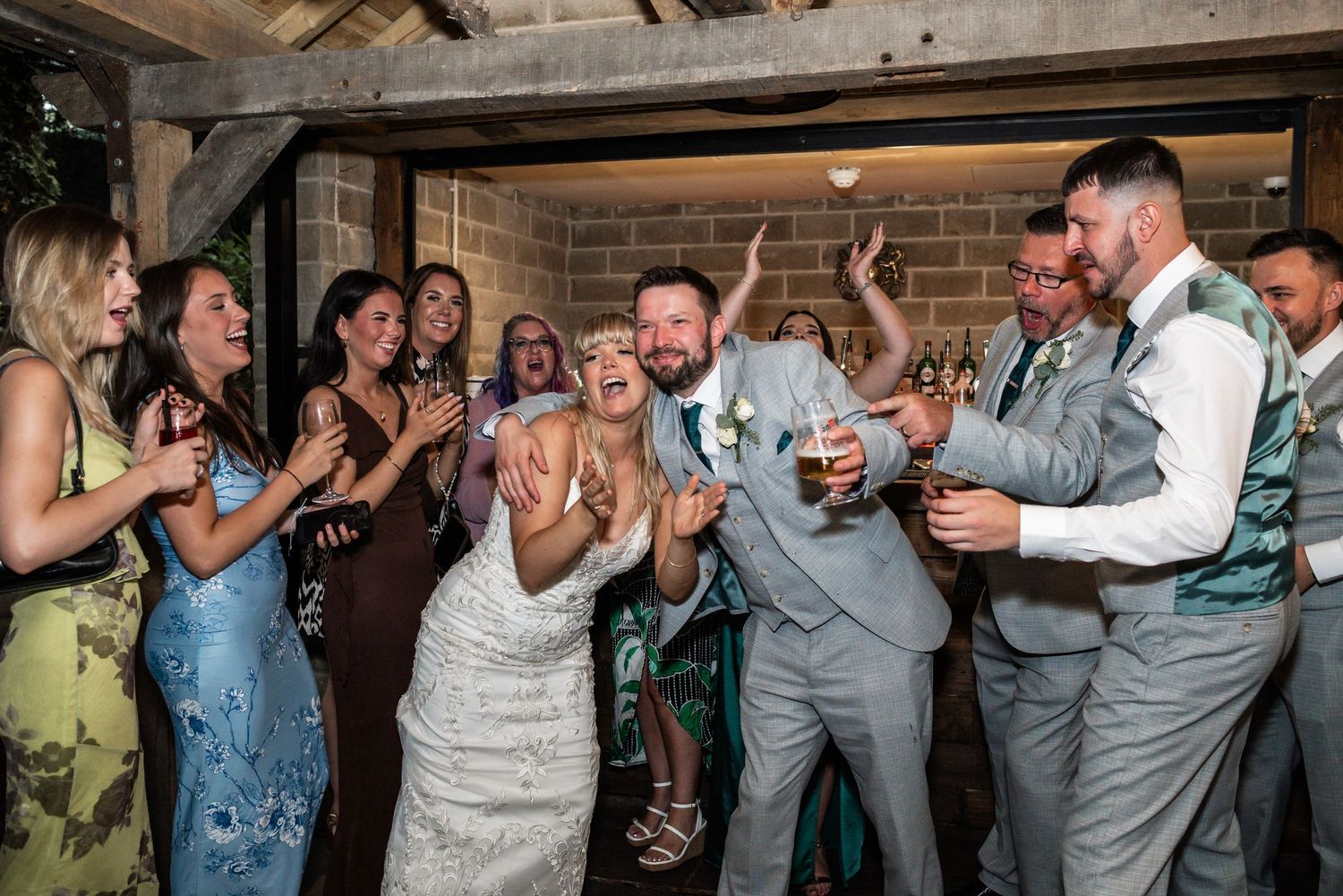 Wedding reception dance party scene with guests celebrating in formal attire on a rustic wooden dance floor.