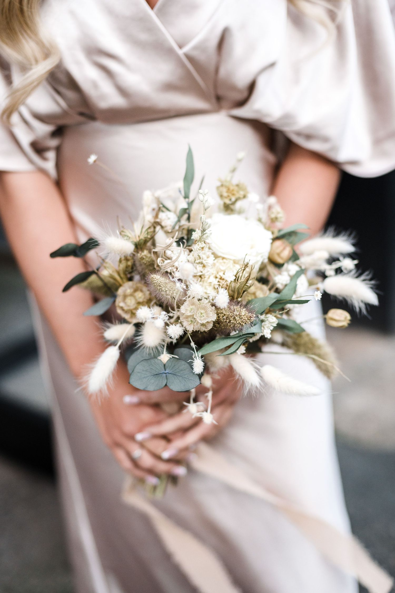 Close-up of dried flower wedding bouquet held against cream silk dress.