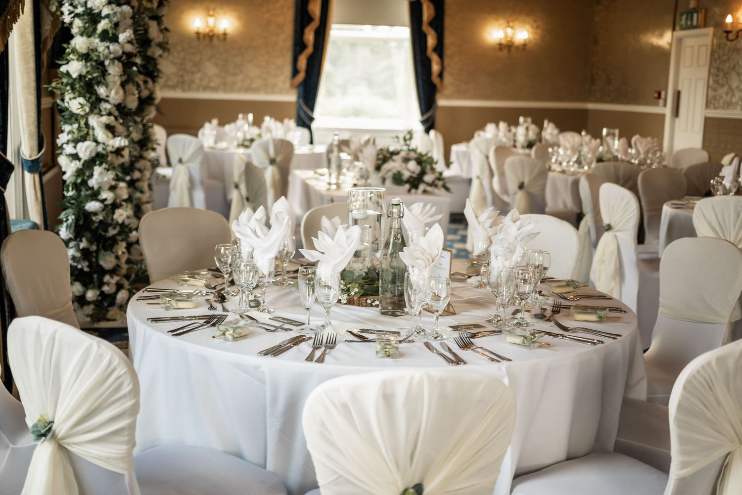 Elegant wedding reception table setting with white linens and floral centerpieces.
