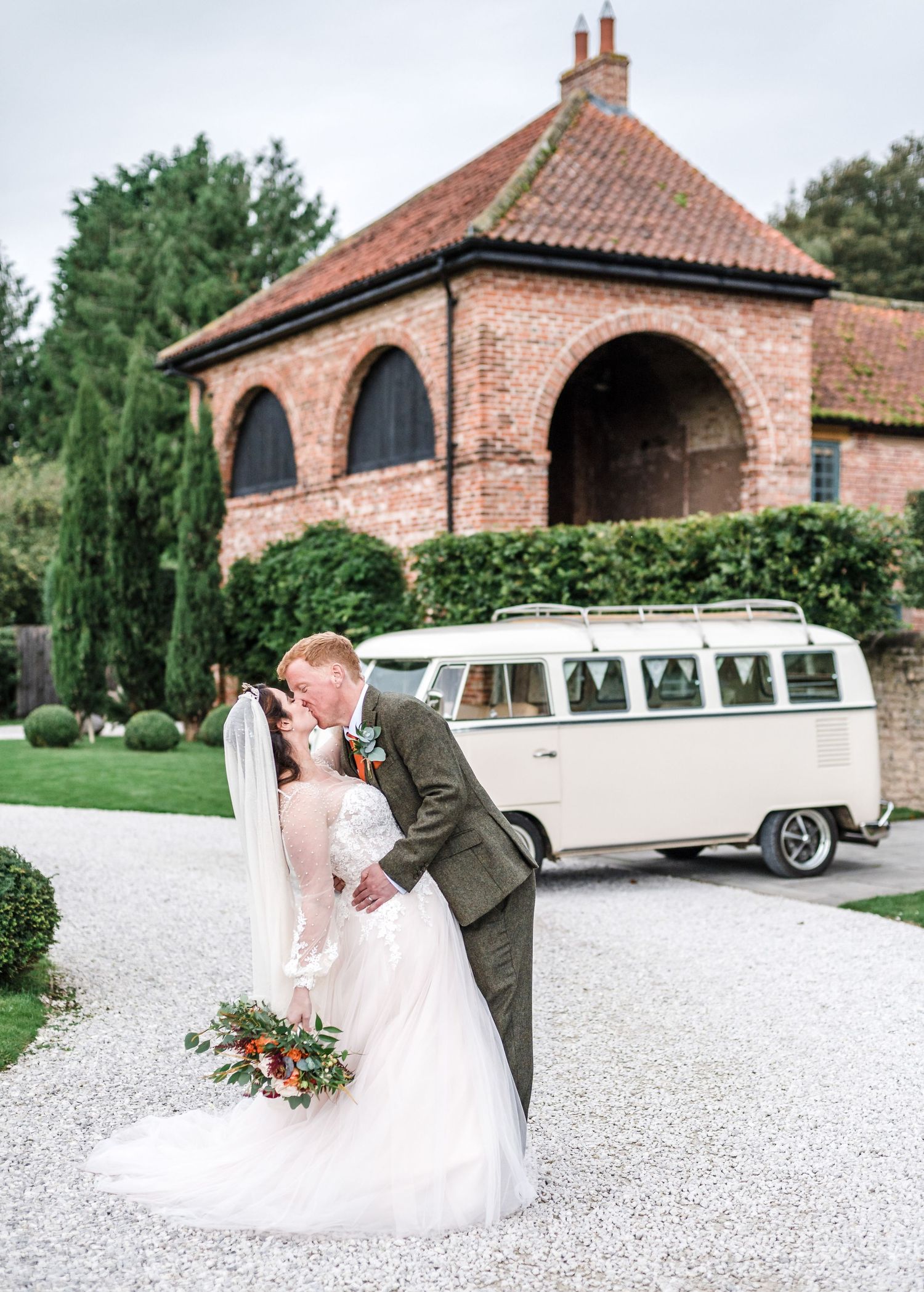 Romantic wedding portrait in front of brick building with classic VW van in background.