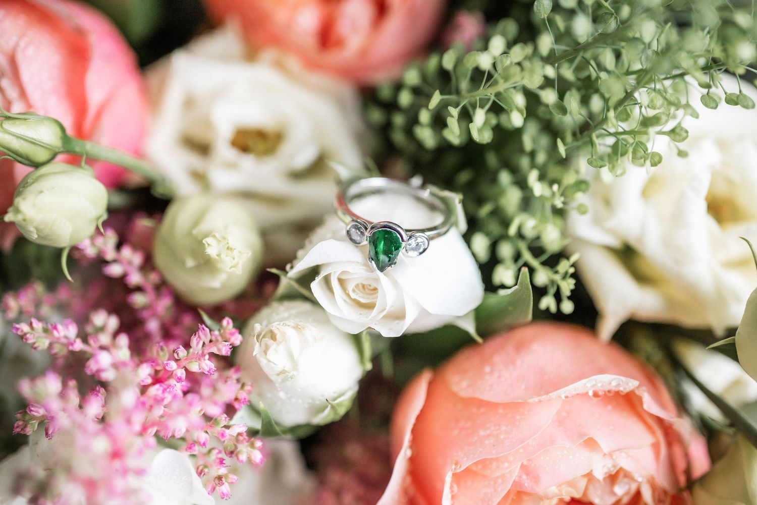 Close-up of wedding bouquet with coral and white roses, delicate baby's breath, and engagement ring.