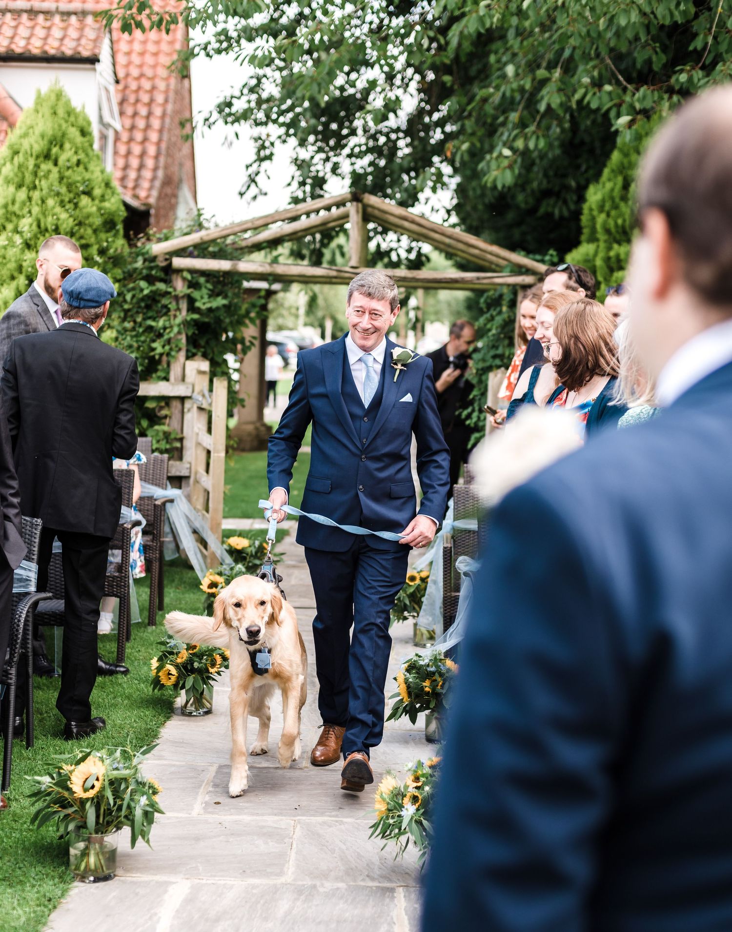 Wedding ceremony exit with couple and dog walking down decorated garden path.
