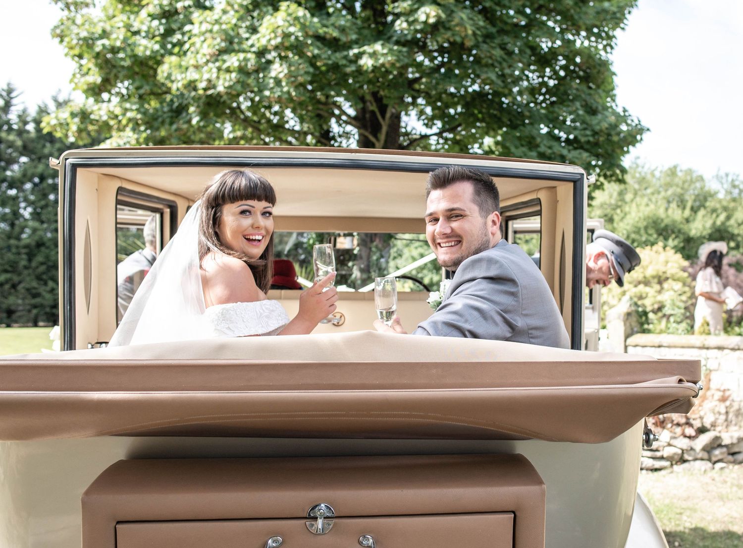 Newlyweds smile while seated in their vintage wedding car.