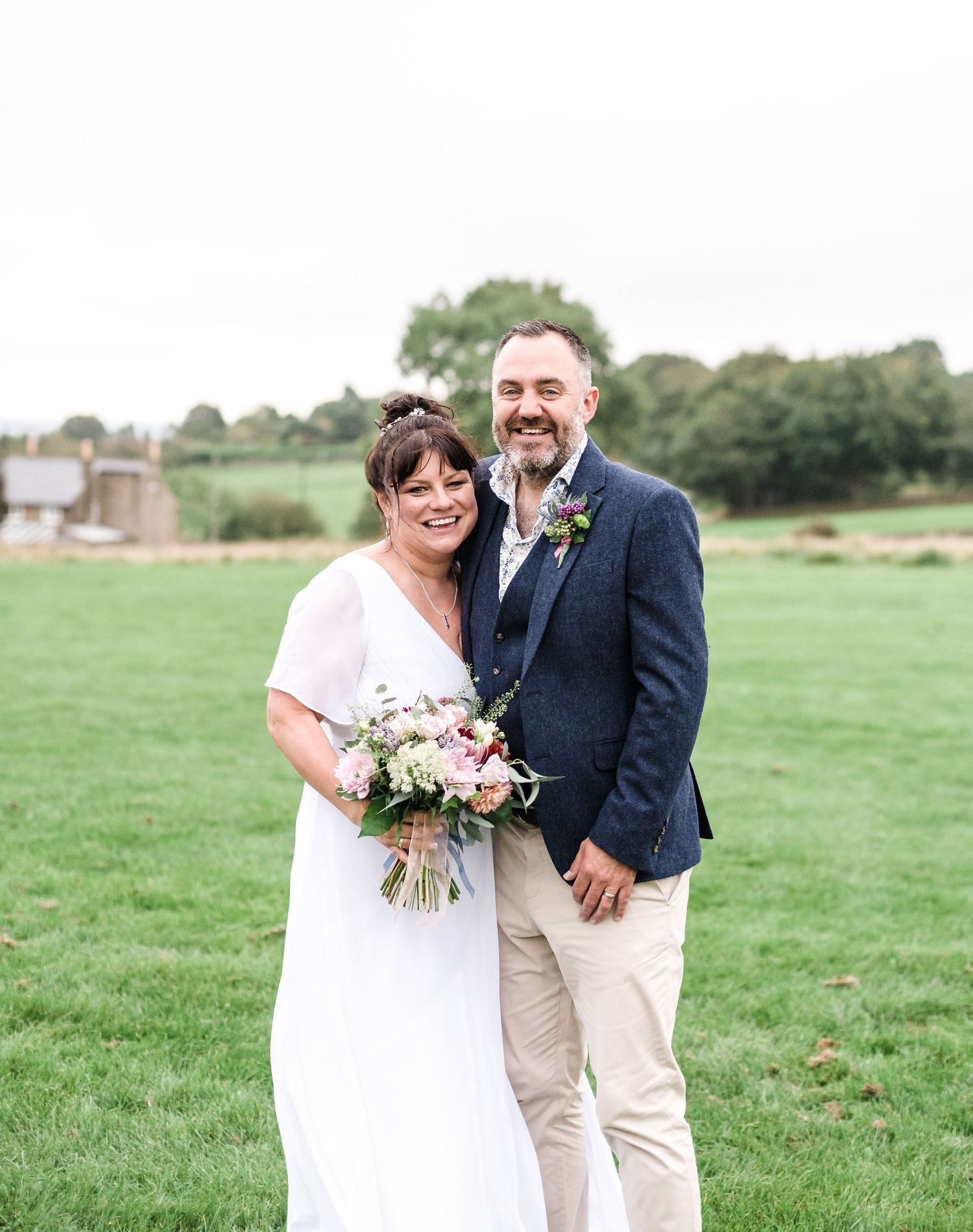 A beautiful outdoor wedding portrait showing a couple on a grassy field with the bride holding a floral bouquet.