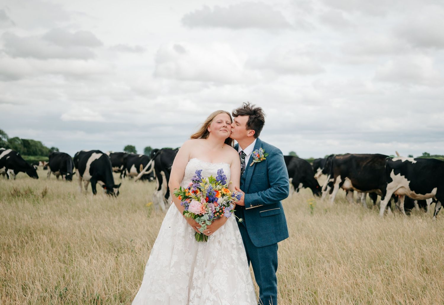 Wedding couple posing together in golden field under cloudy sky.