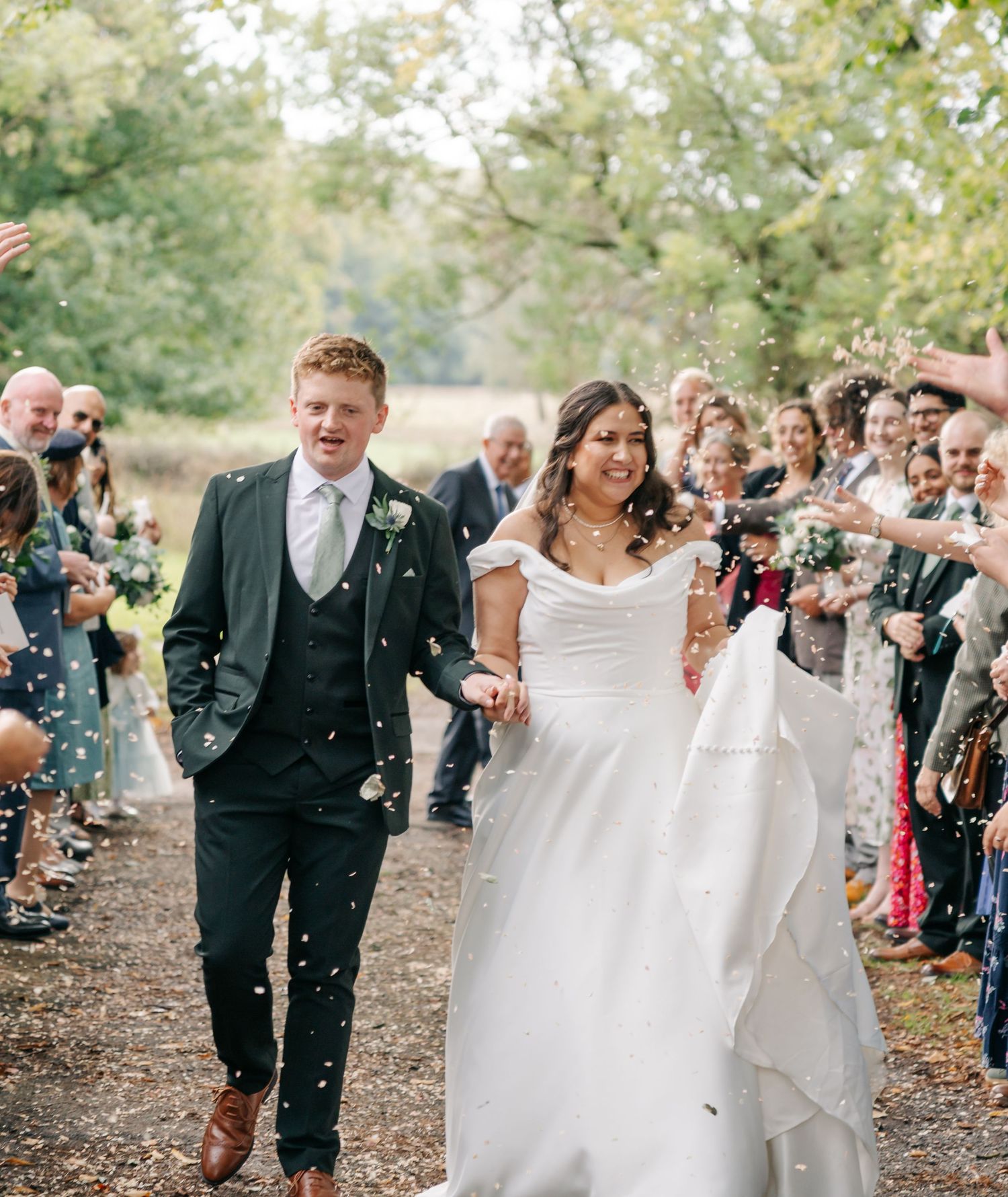 Wedding guests shower the newlyweds with confetti as they walk down a tree-lined path during an autumn celebration.