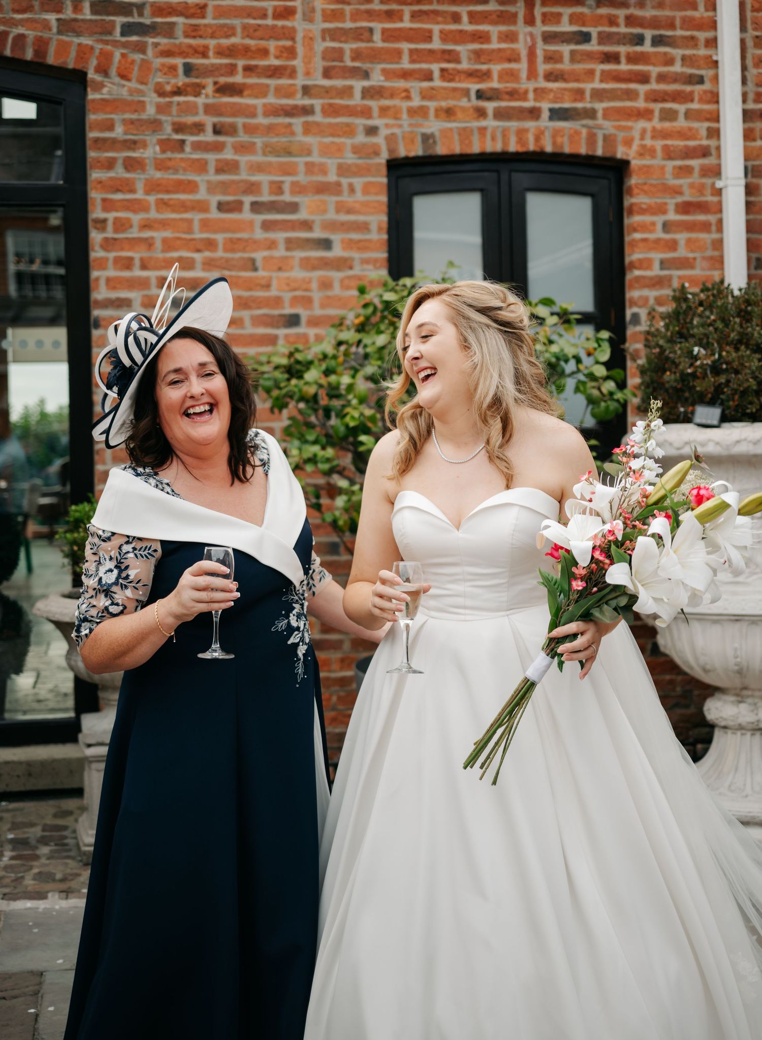 Bridesmaids in navy dresses and bride in white gown sharing joyful laughter while holding champagne glasses.