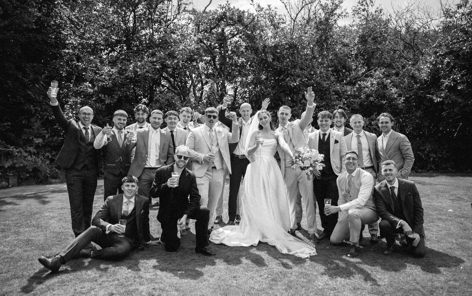 Wedding party poses together for outdoor group photos in a natural garden setting.