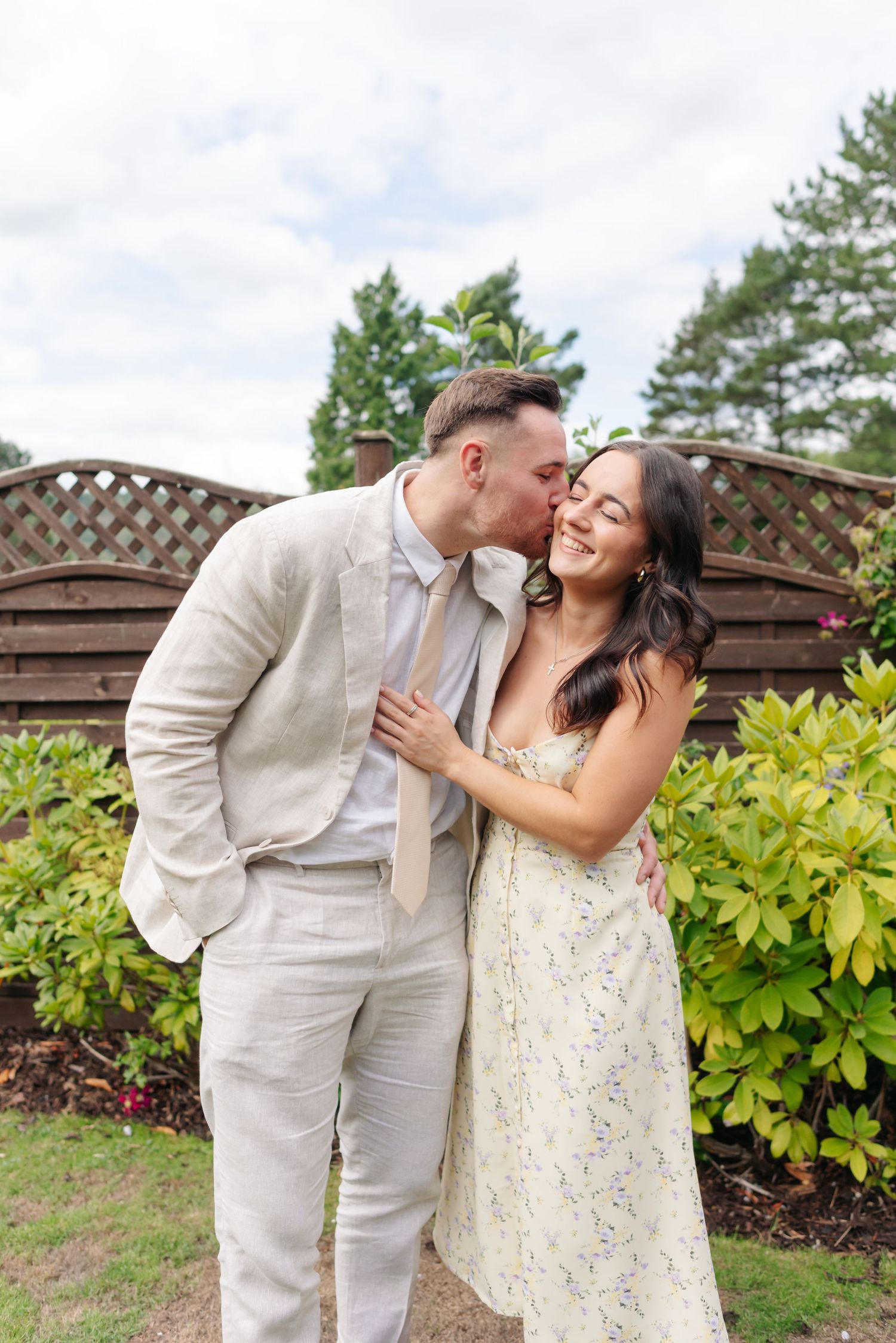 Couple shares intimate moments in a garden setting with wooden lattice and greenery.