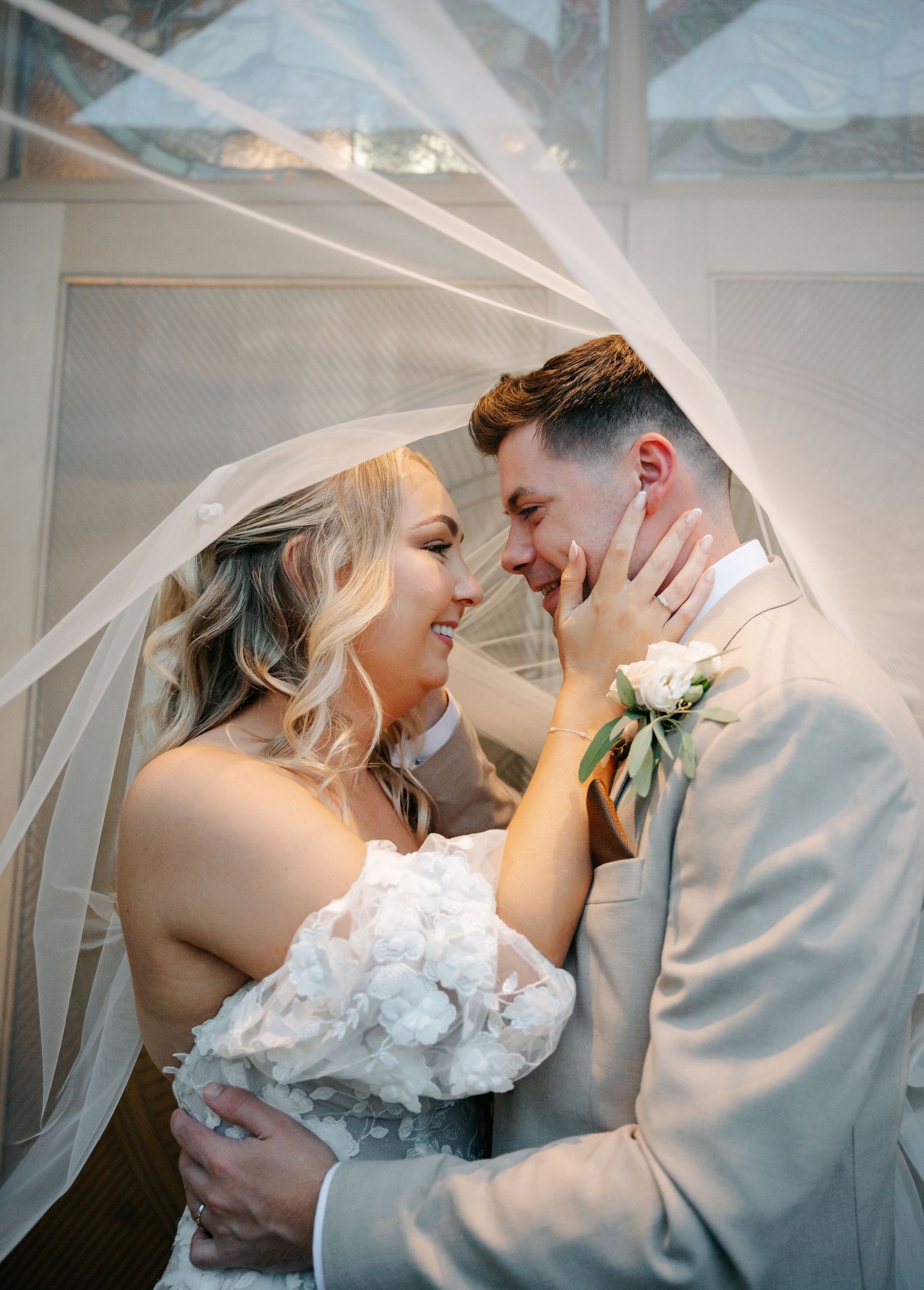 A romantic moment under flowing veil fabric as a couple shares an intimate embrace at their wedding.