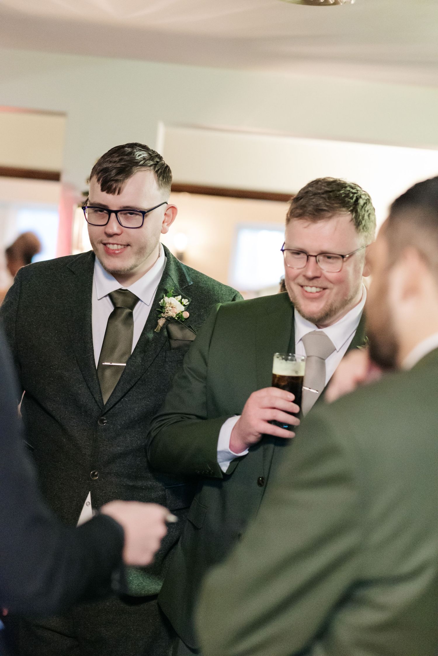 Groomsmen in dark suits share laughs and drinks during a wedding celebration.