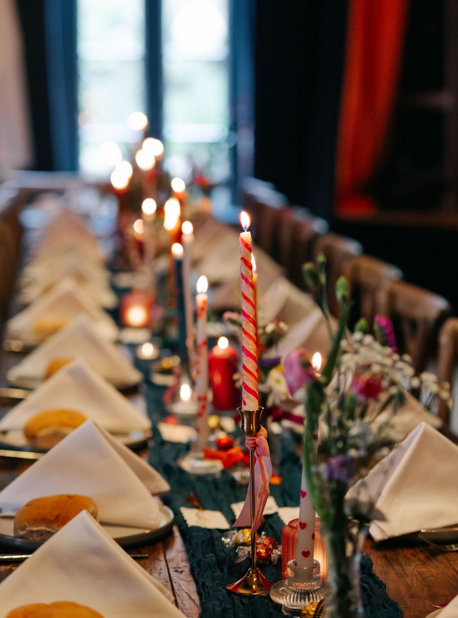 Elegant wedding table setting with candles, greenery and white napkins on dark tablecloth.