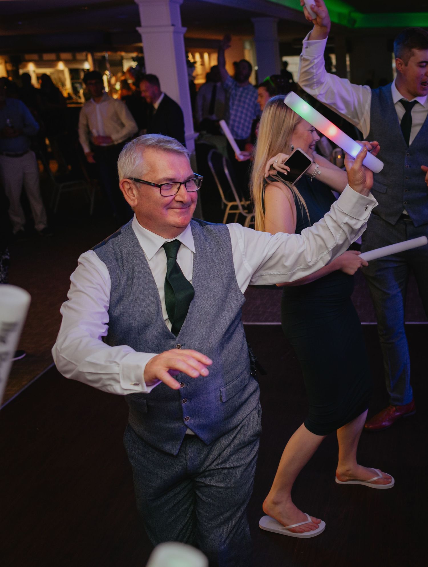 Wedding guests dance enthusiastically on a dimly lit reception dance floor.