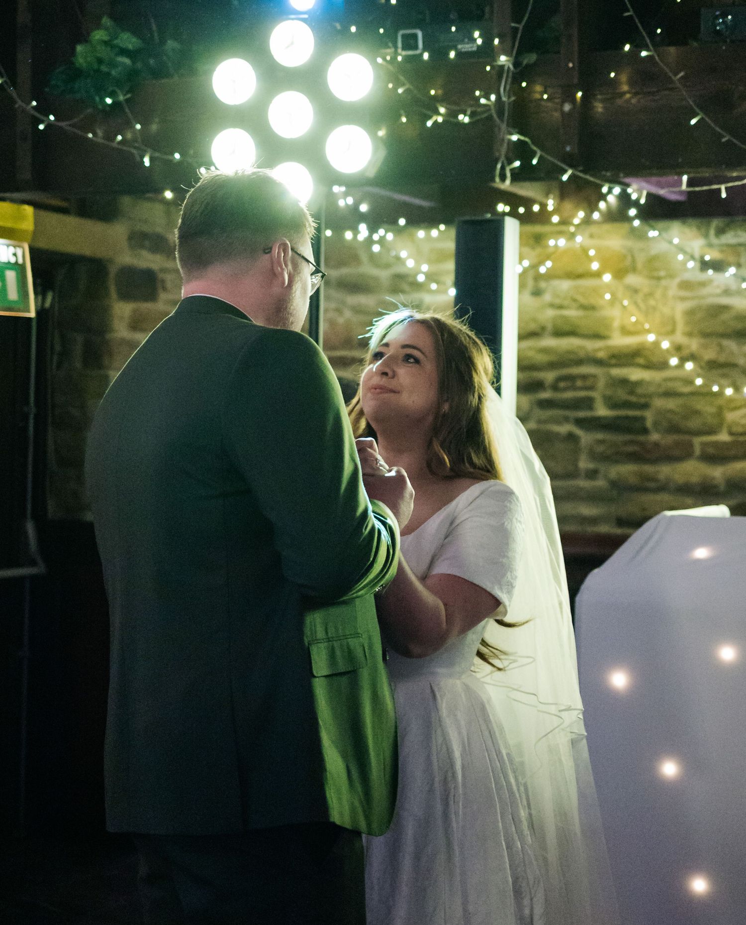 First dance under twinkling lights at an intimate stone-walled wedding reception.