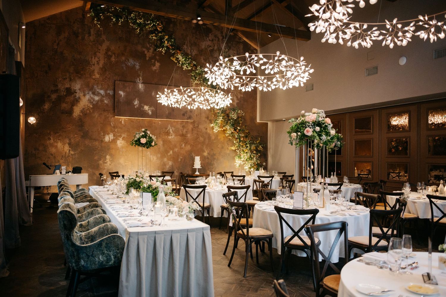Wedding reception room with elegant white table settings and overhead string light decorations.