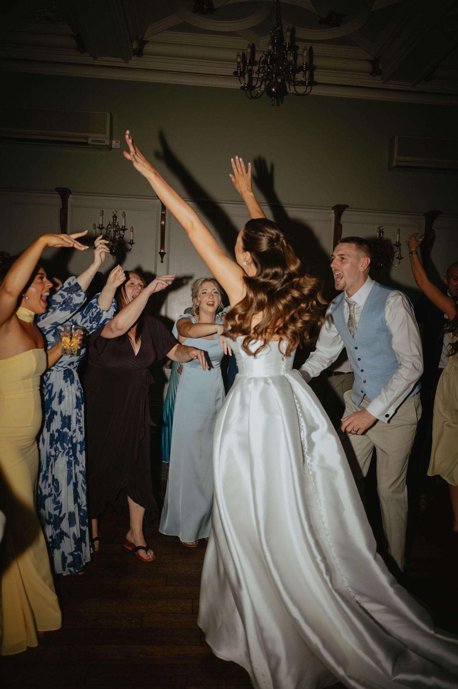 Wedding reception dance party with guests dancing energetically under dimmed lighting.