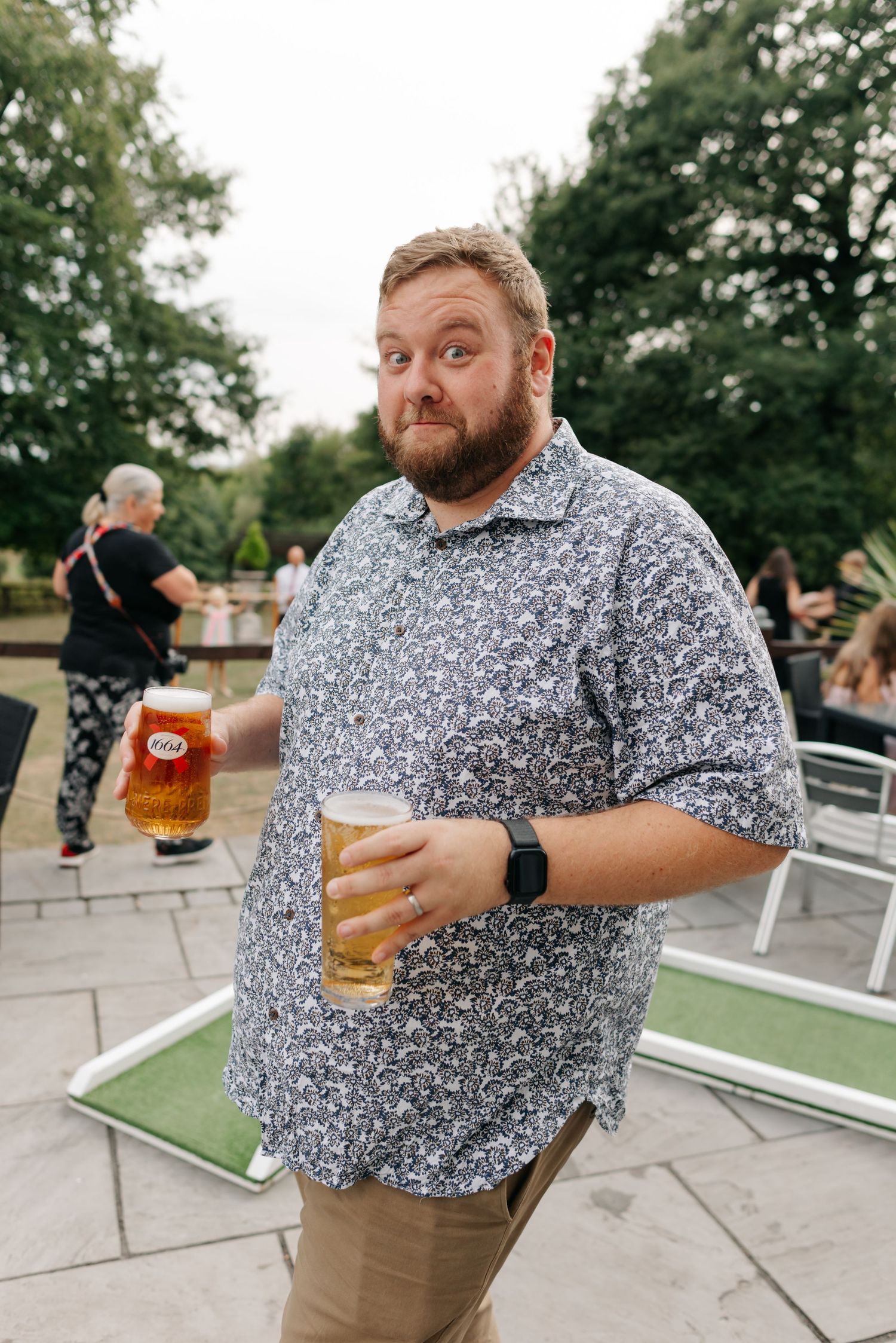 A guest in a patterned shirt enjoys a beer at an outdoor wedding reception.