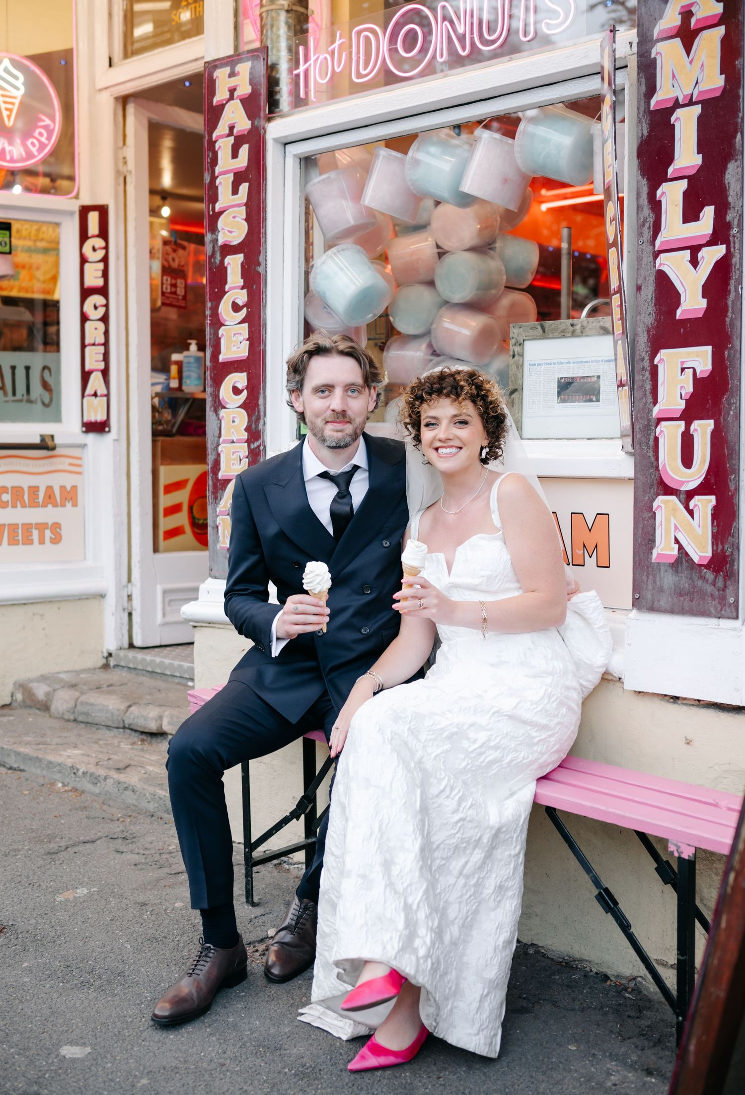 Newlyweds pose for fun photos outside a retro donut shop with pink accents.