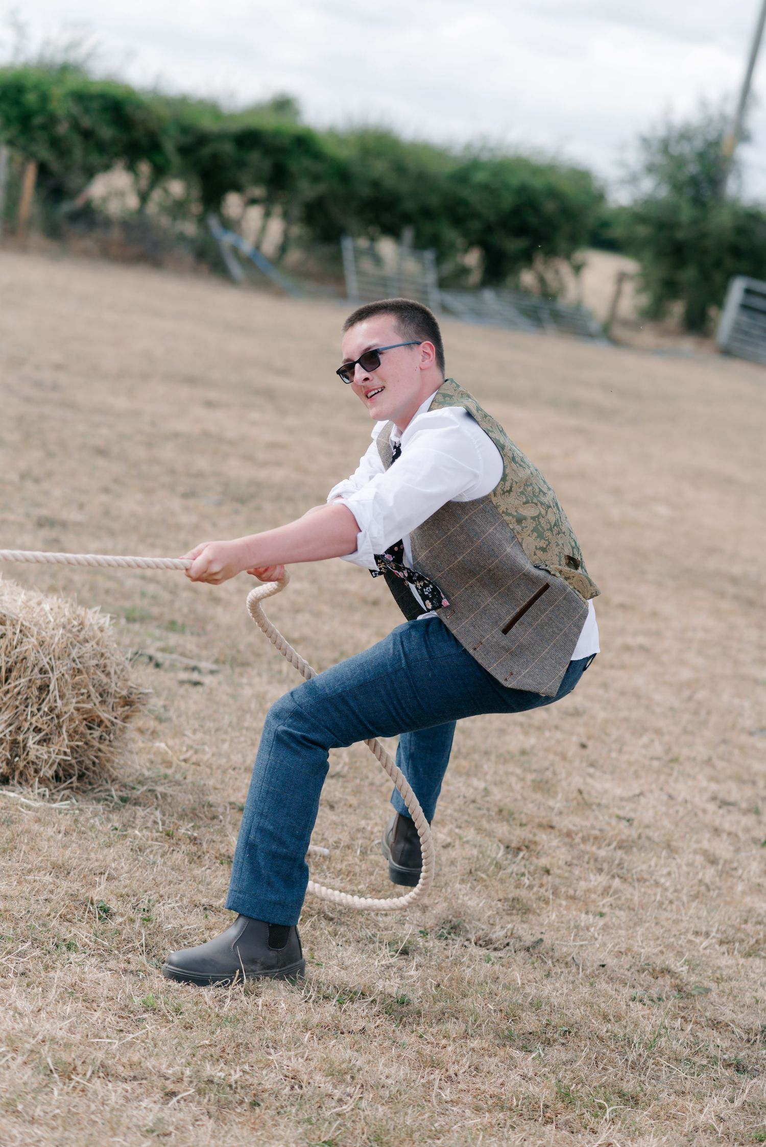 A person in a tweed vest and jeans performing dramatic dance moves in an outdoor field.