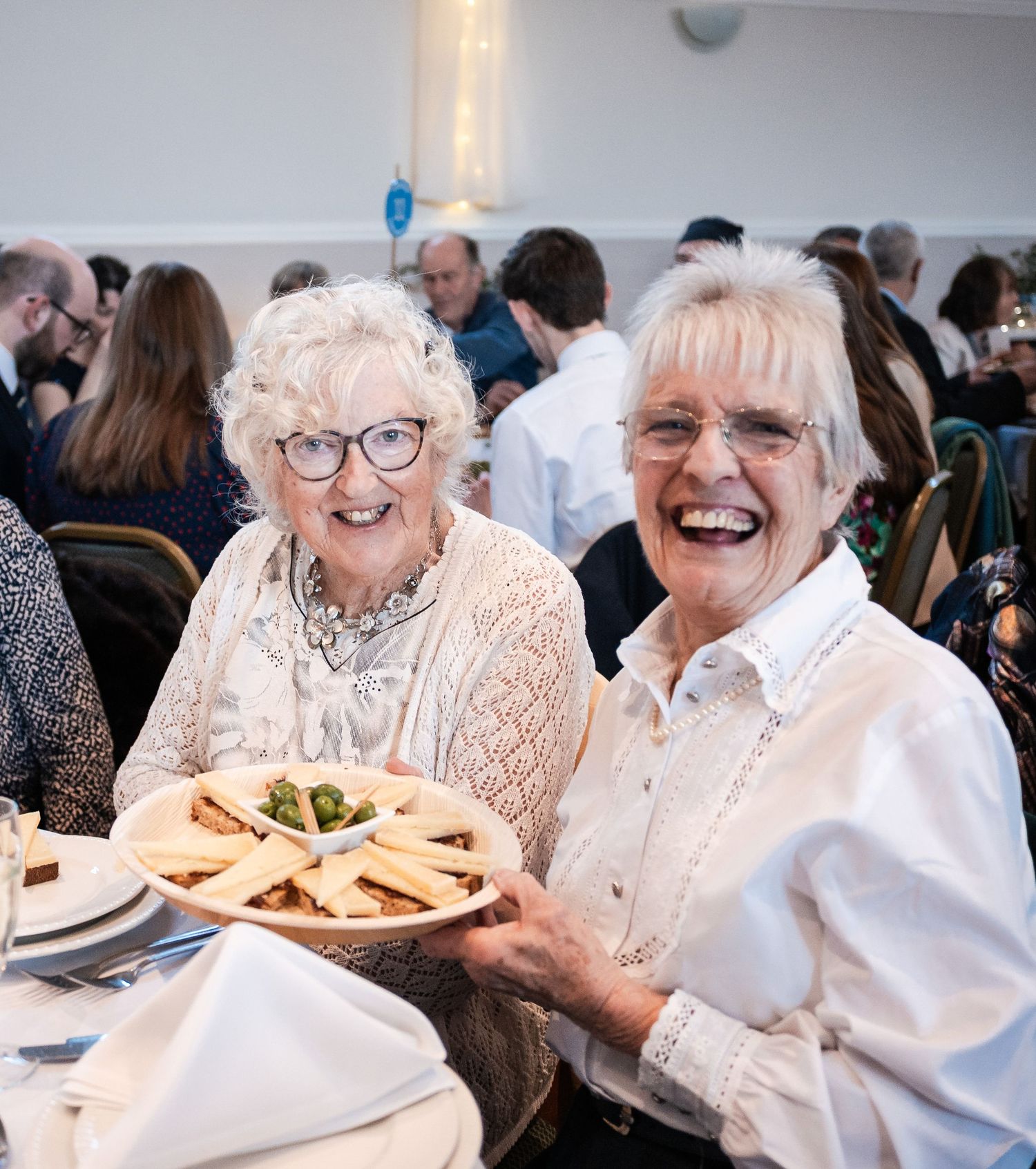 Seniors enjoying a festive meal together at a social gathering with plates of food and laughter.