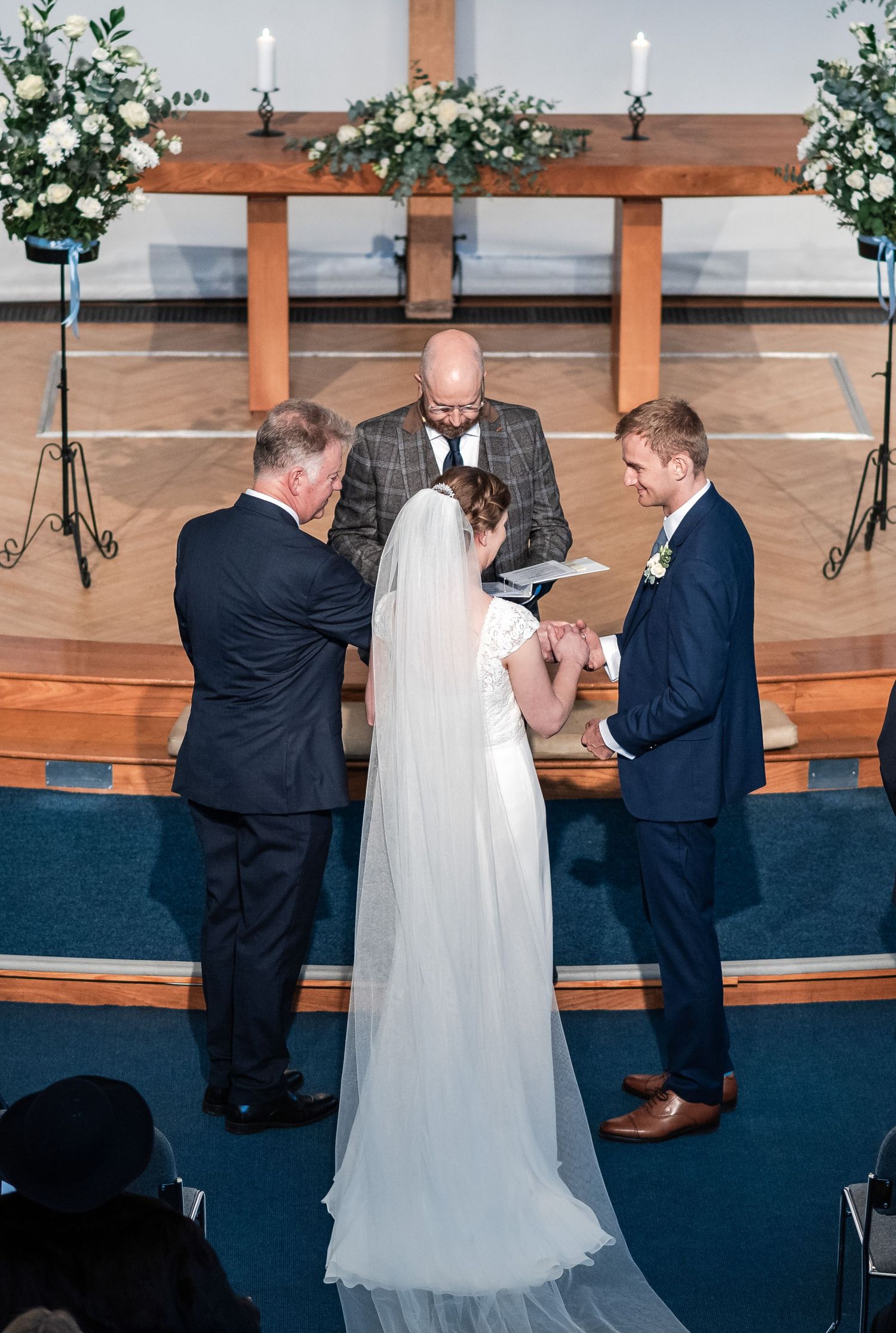 Wedding ceremony in progress at a church altar with wooden beams and white floral decorations.