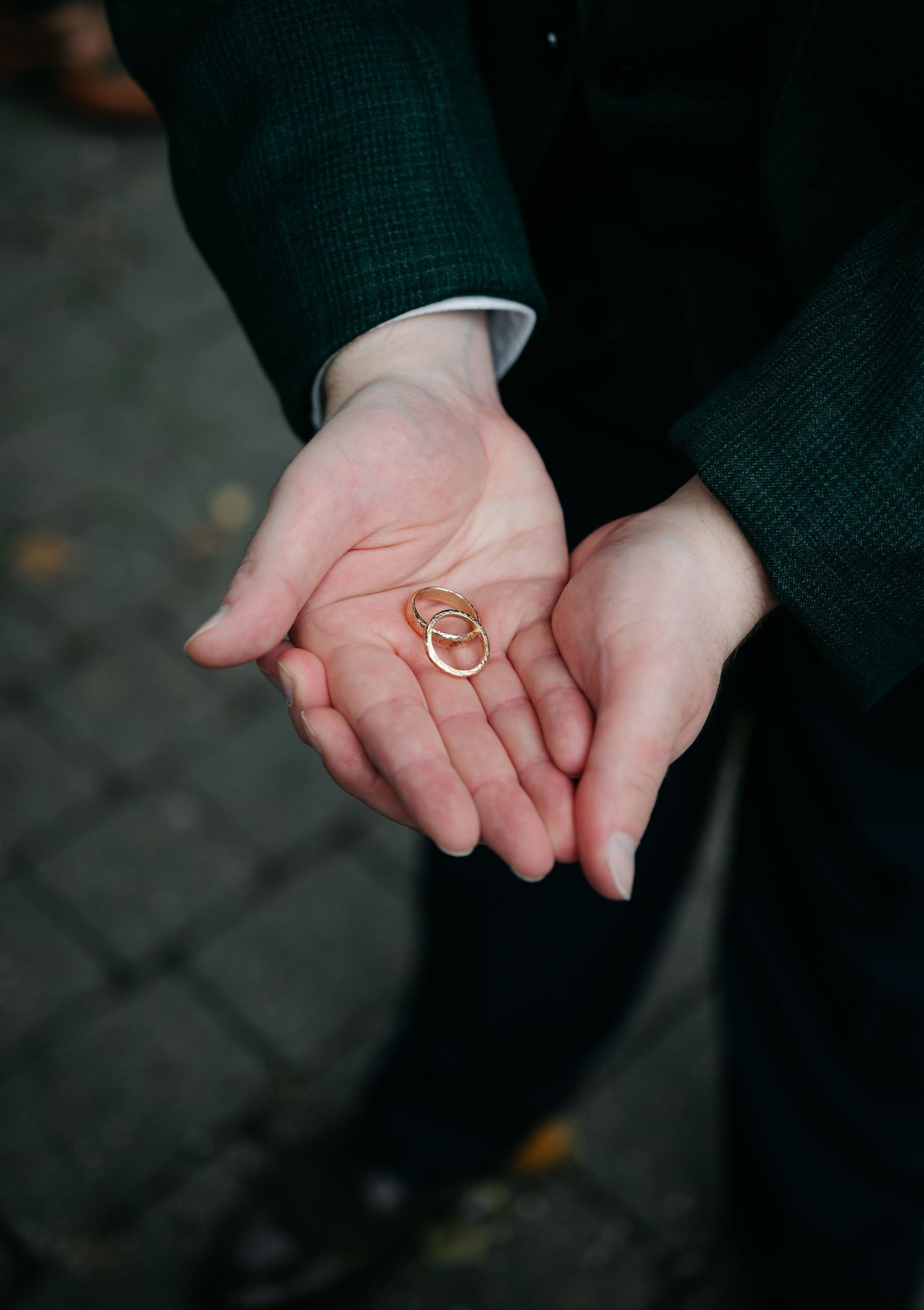Close-up of hands holding gold wedding rings against a dark background.