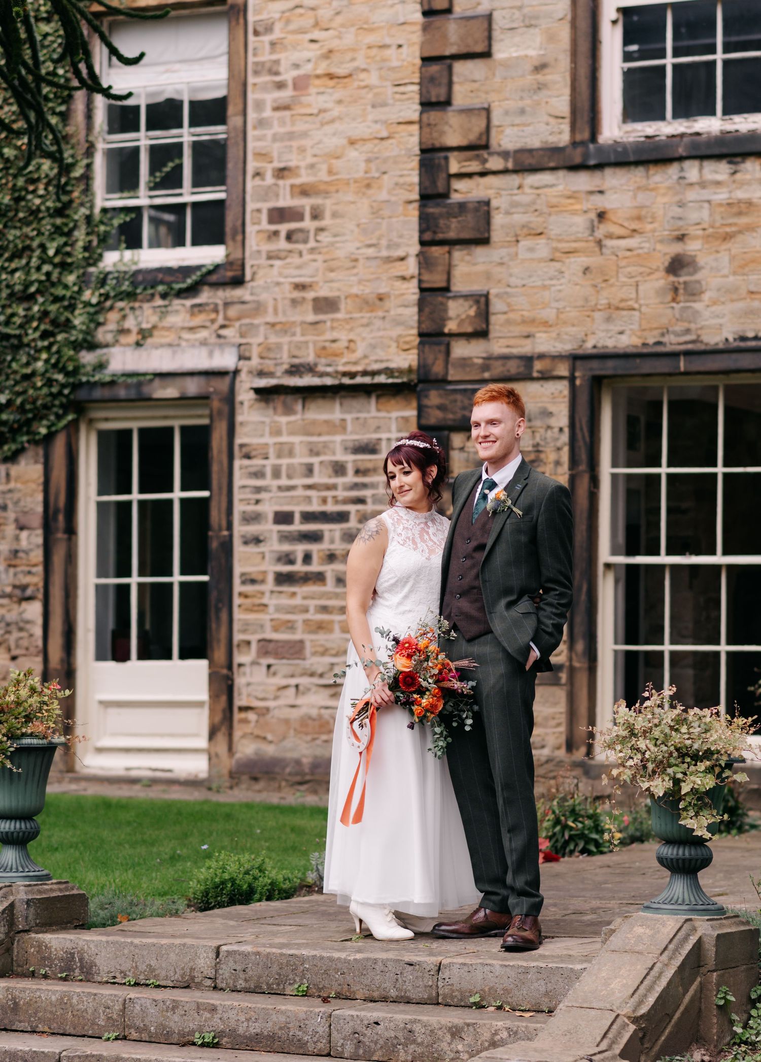 Couple taking wedding portraits outside historic stone building with large windows.