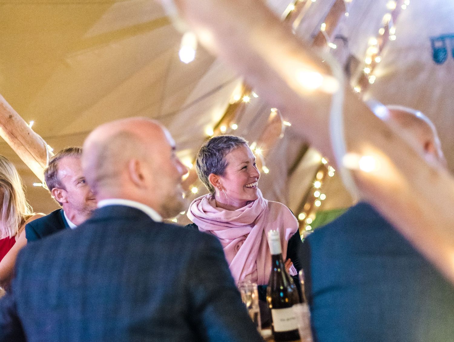 Wedding guests mingling during a reception under decorated tent lighting.
