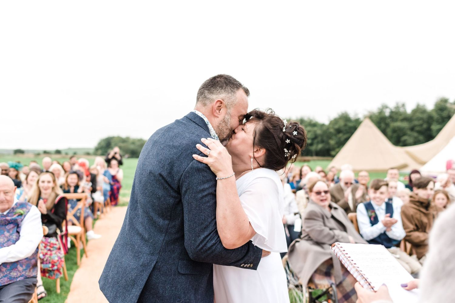 Wedding ceremony celebration with guests watching a couple embrace outdoors near a teepee tent.