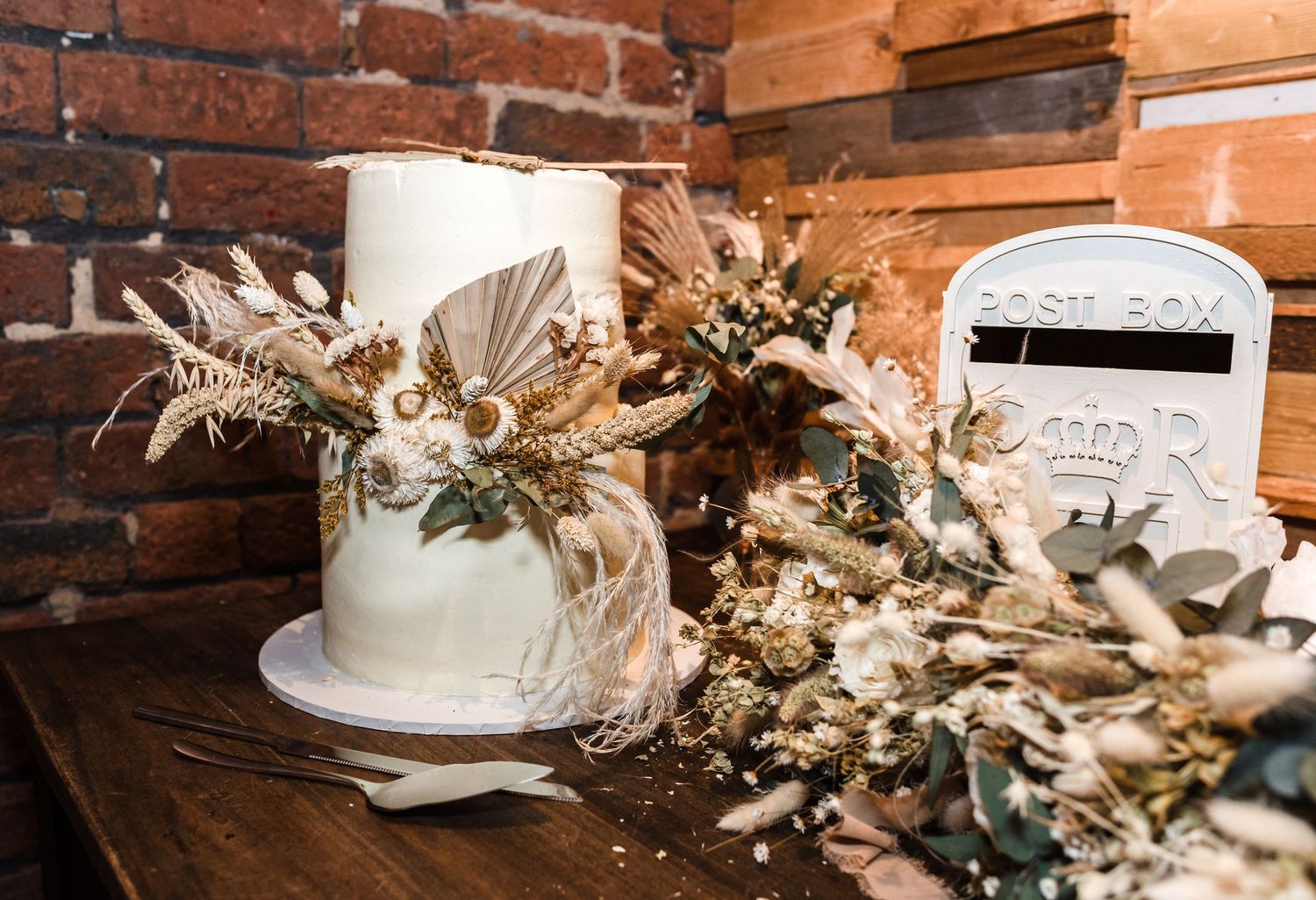 An elegant white wedding cake decorated with dried flowers sits on a rustic wooden table.